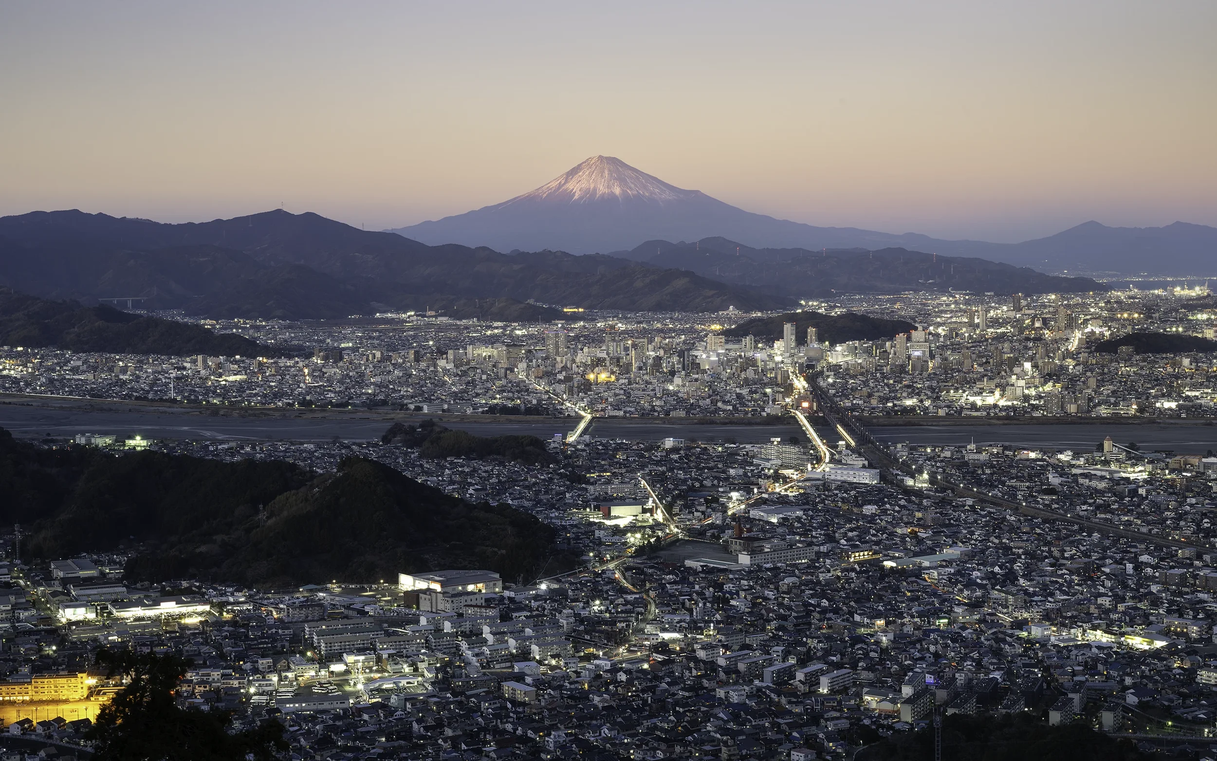 As twilight settles over Shizuoka, the city lights slowly awaken beneath Mount Fuji. The contrast between urban life and Japan's highest mountain reflects one of the country's defining landscapes.