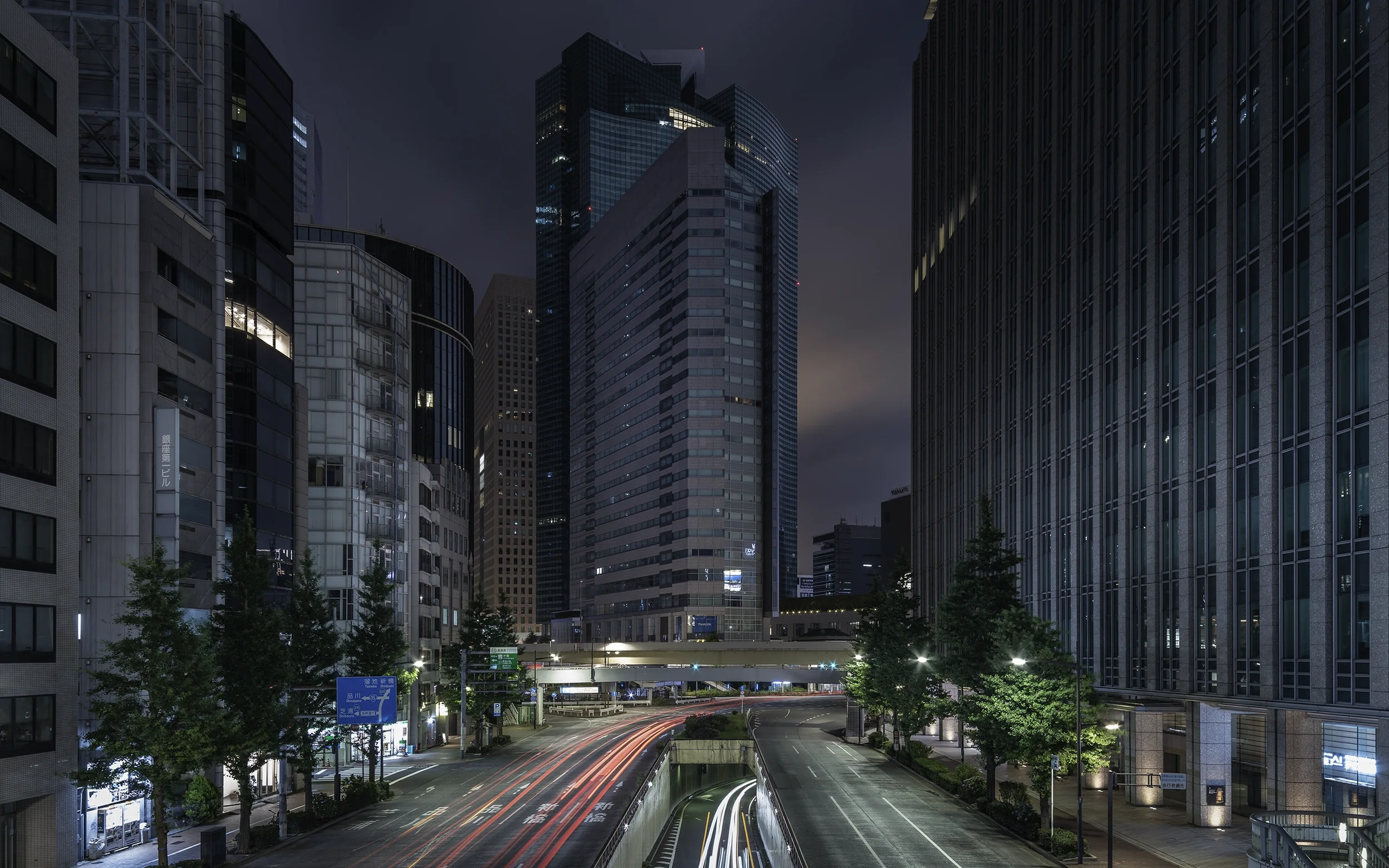 Vue urbaine nocturne avec des gratte-ciel modernes, des rues vides et des feux de circulation laissant des traînées de lumière.
