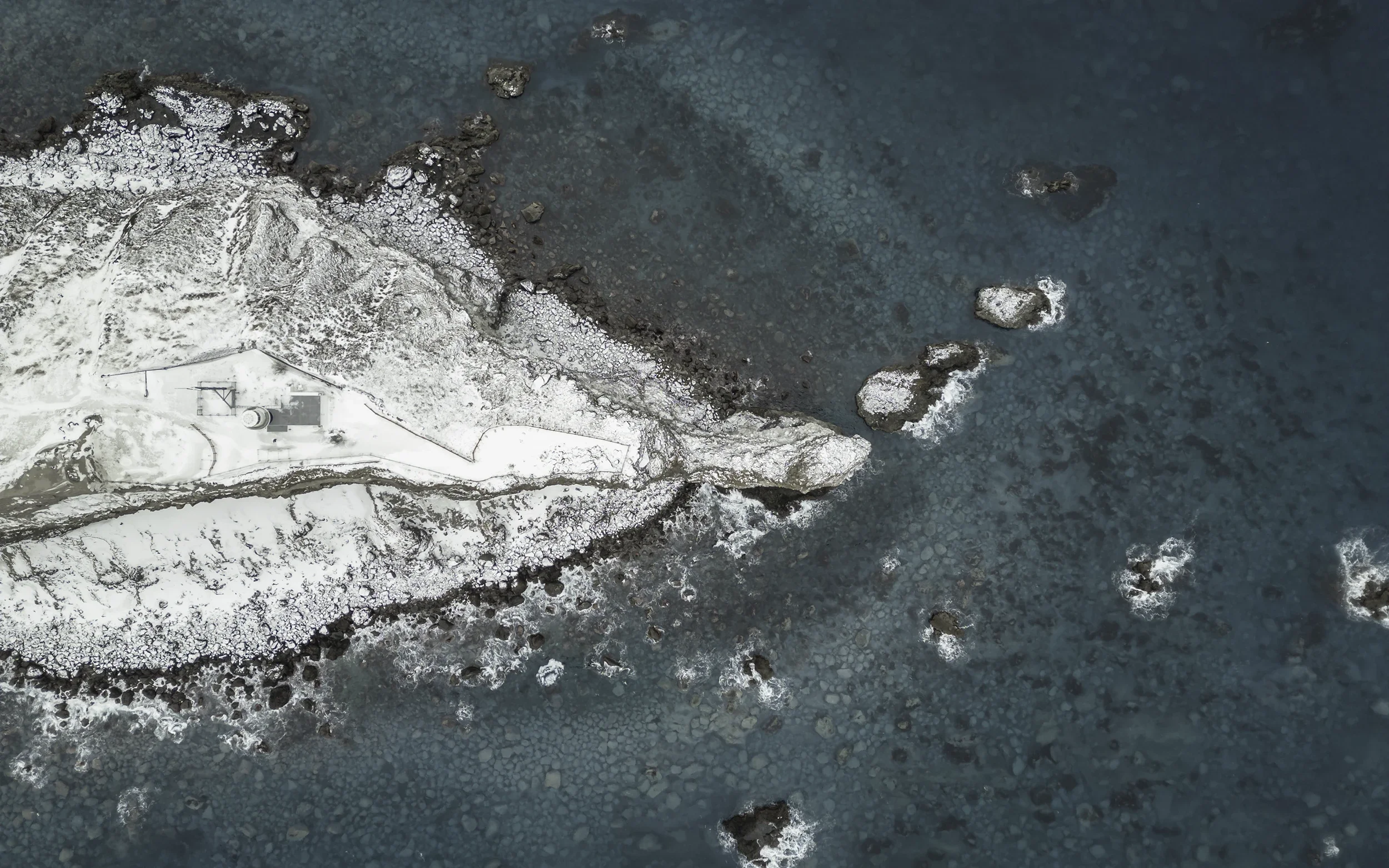 Aerial view of Cape Kamui on the Shakotan Peninsula in Hokkaido, where turquoise waters meet a snow-covered rocky coastline.