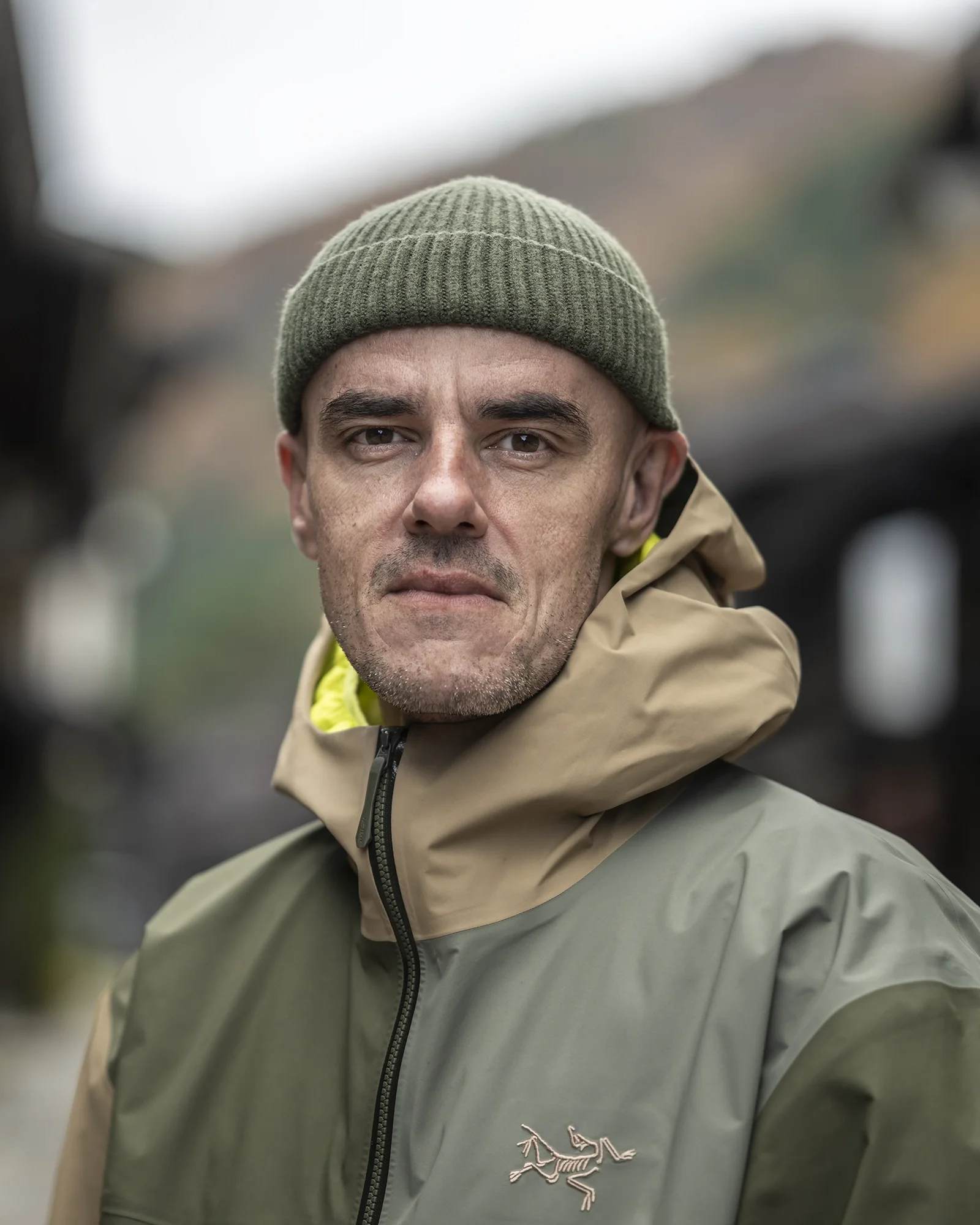 Homme portant un bonnet vert et une veste beige et vert, en extérieur.