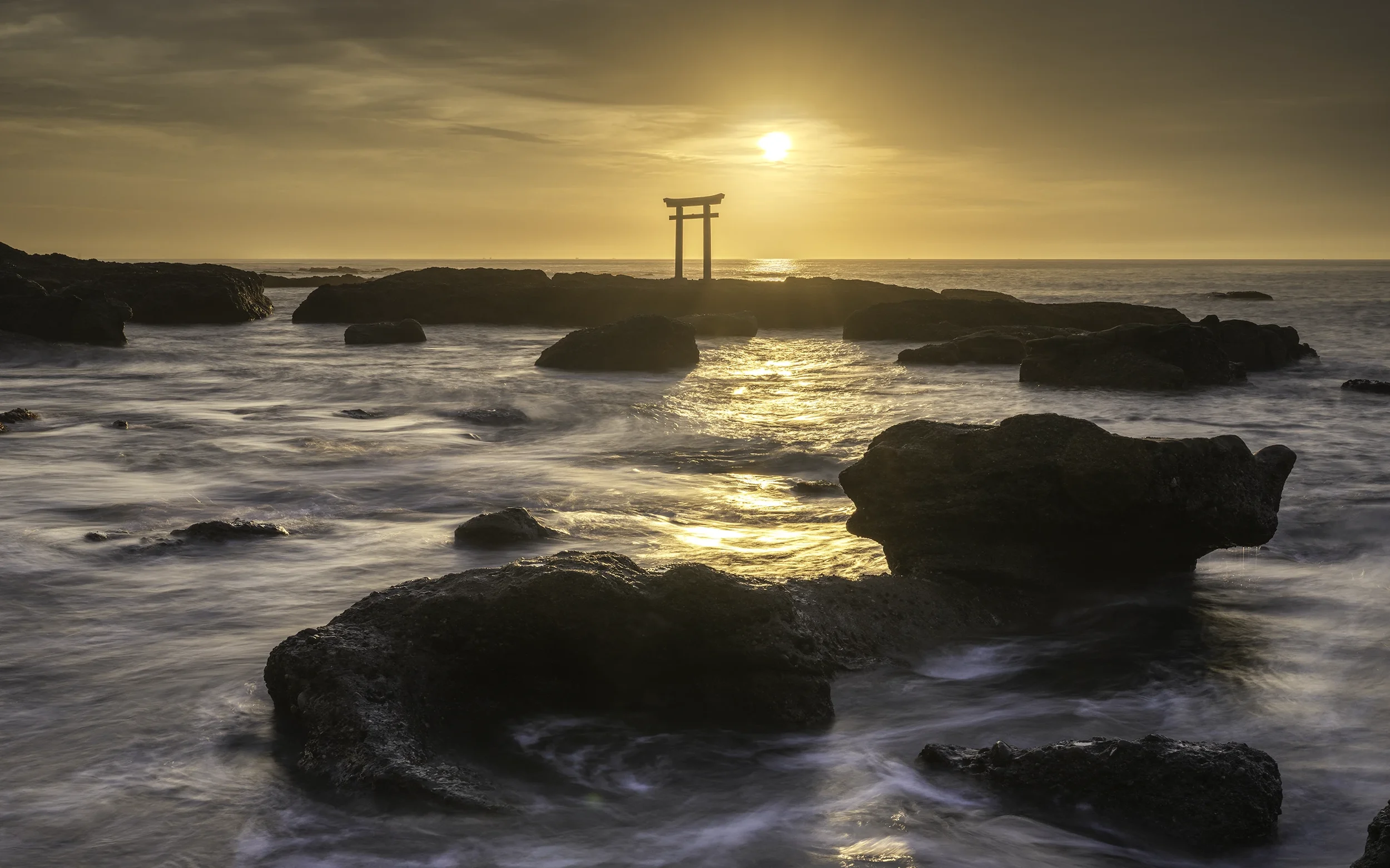 Coucher de soleil sur une mer avec des rochers et une porte torii au loin.