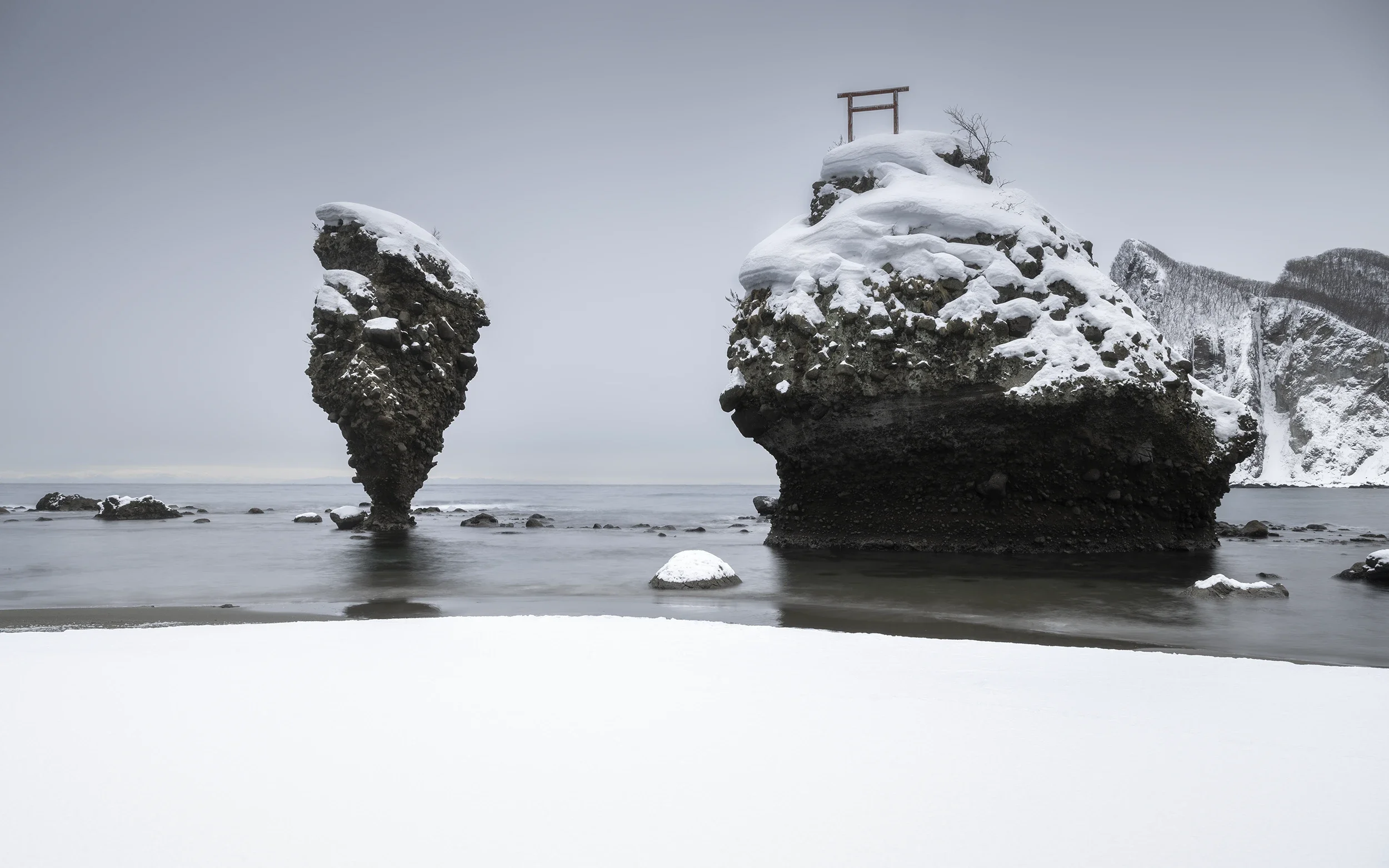 now-covered Ebisu Rocks rising from the Sea of Japan on the Hokkaido coast during a calm winter morning.