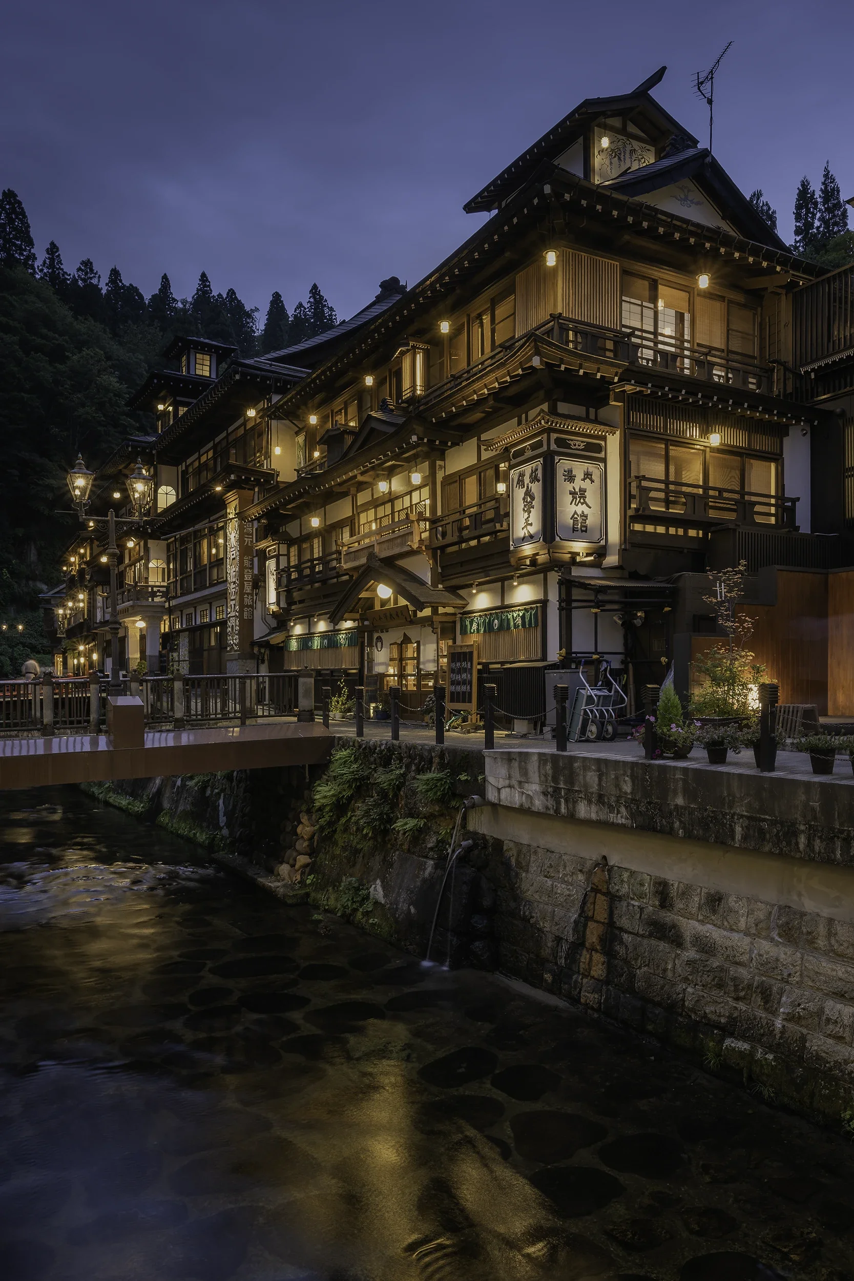 Traditional ryokan line the Ginzan Onsen river at dusk, creating one of Japan's most iconic hot spring towns with glowing lanterns, wooden buildings and timeless atmosphere.