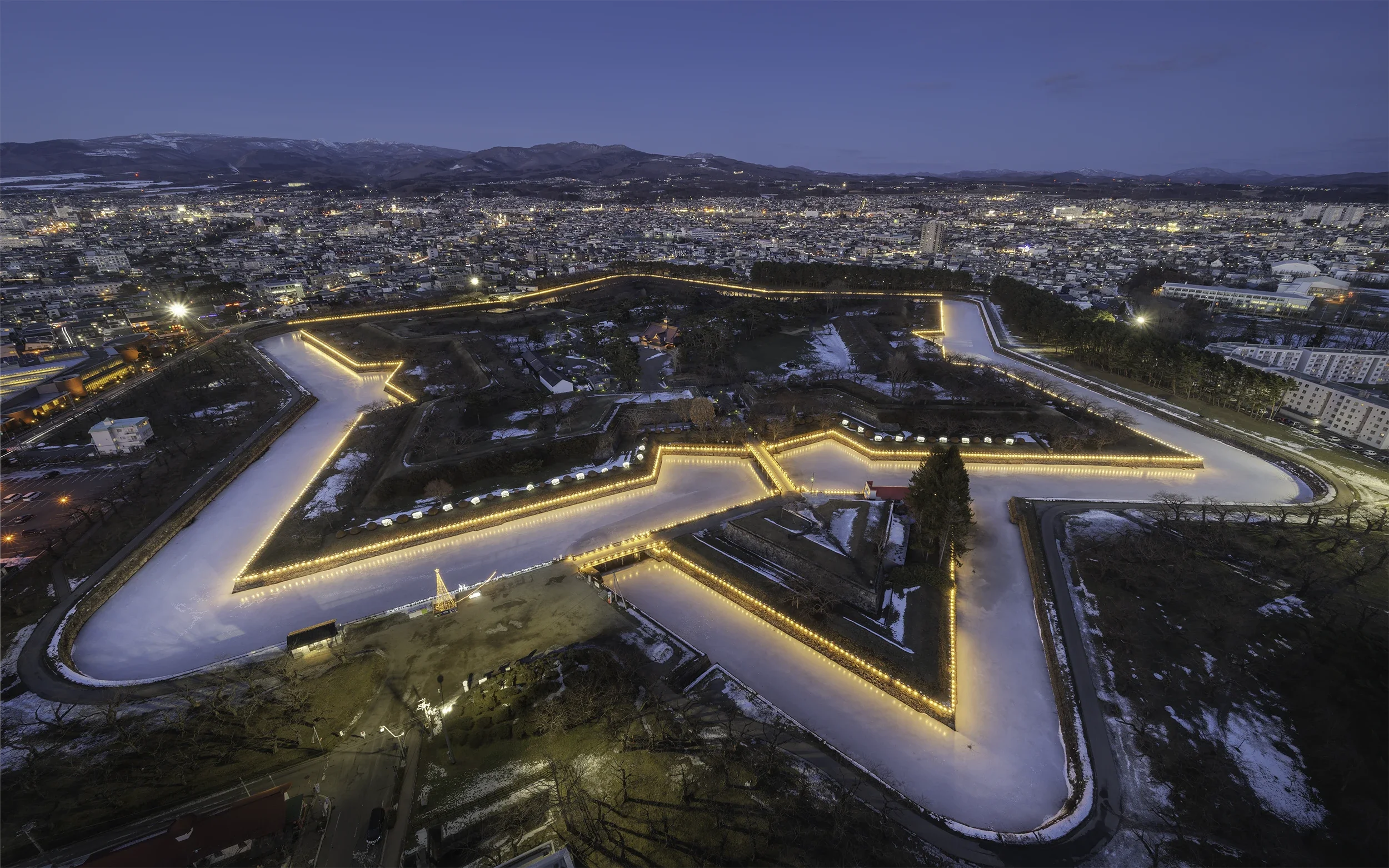 Aerial night view of Goryokaku Fort in Hakodate, Hokkaido, illuminated during winter with snow covering the historic star-shaped fortress.
