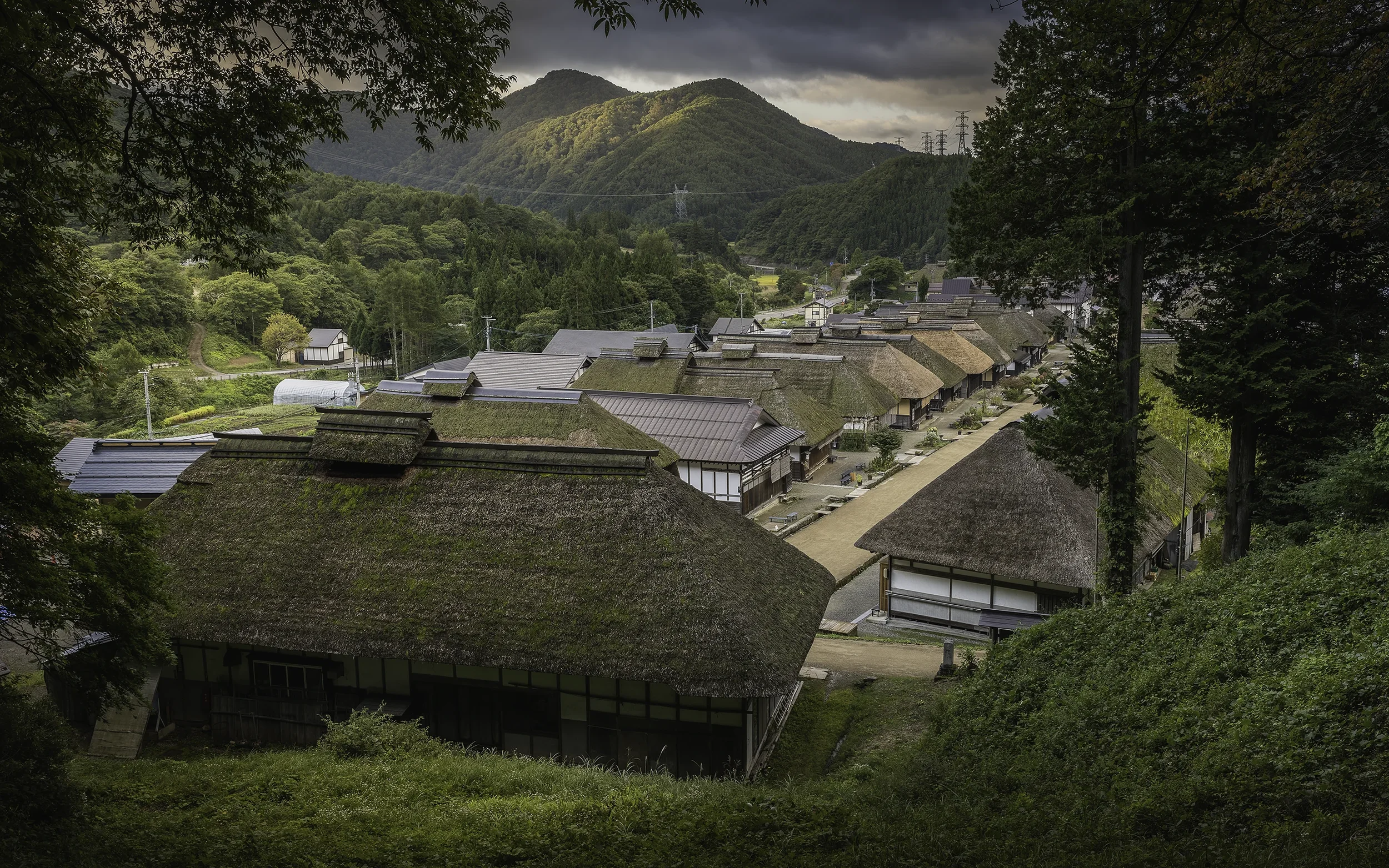 Village traditionnel japonais avec des maisons aux toits en chaume, entouré de montagnes verdoyantes.