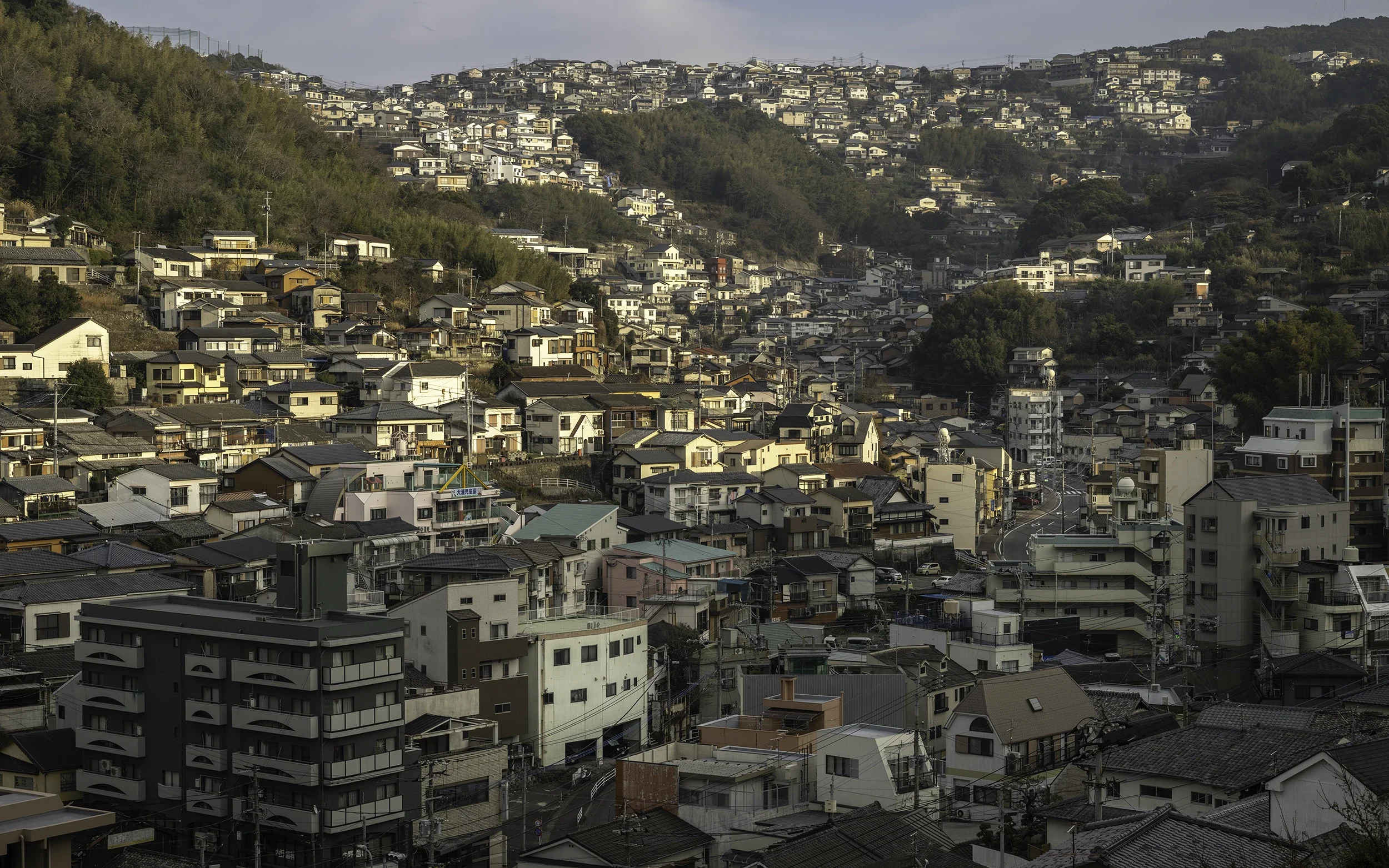 Elevated view of Nagasaki, Japan, revealing hillside neighbourhoods layered across the landscape and overlooking the harbour.
