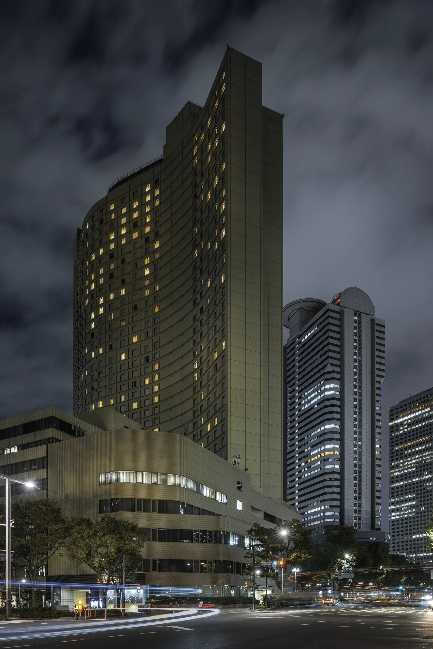 Gratte-ciel modernes illuminés dans une ville la nuit avec des nuages en arrière-plan.