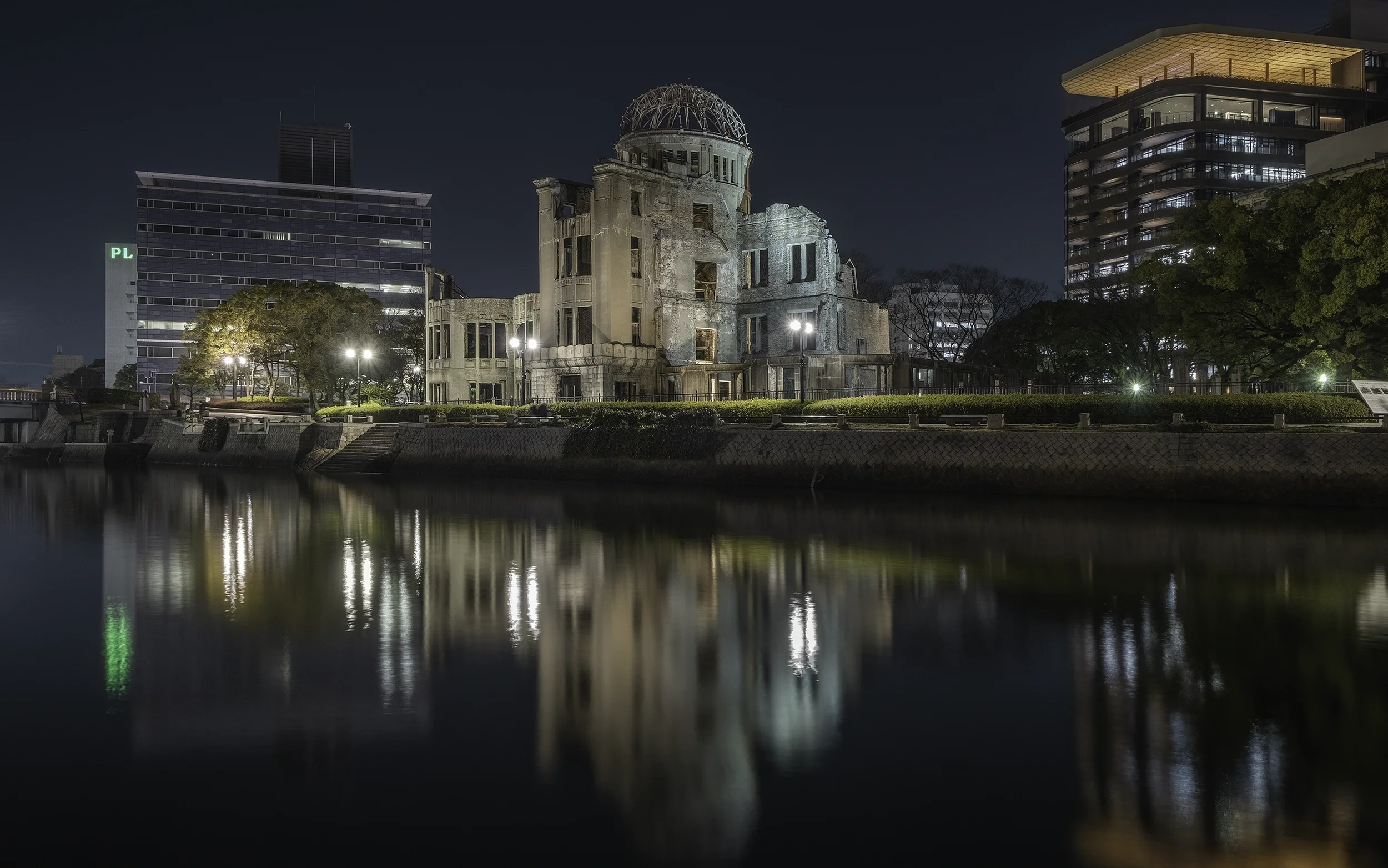 Le mémorial de la paix d'Hiroshima, un bâtiment en ruines, illuminé la nuit, avec des bâtiments modernes en arrière-plan, reflété dans l'eau calmede.