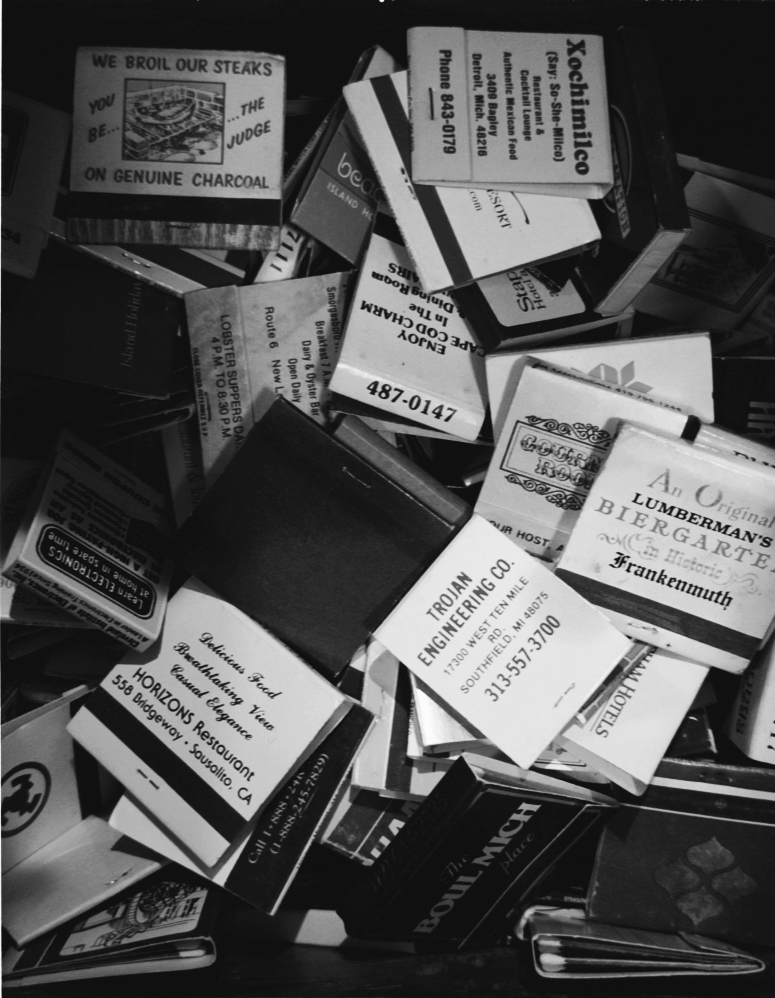 A pile of matchbooks, business cards, and small advertisements, some partially visible, with text advertising various businesses and services.