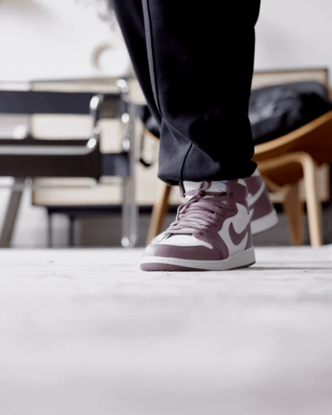 Close-up of a person's foot wearing a pink and white Nike sneaker, standing on a white surface in a room with chairs.