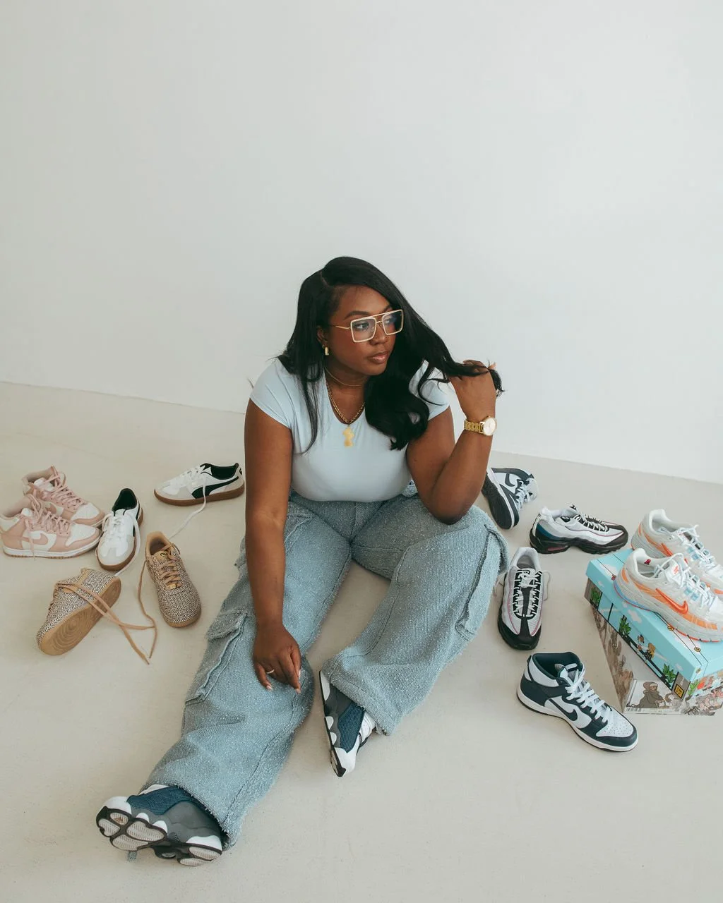 Woman sitting on the floor surrounded by various sneakers and shoe boxes.