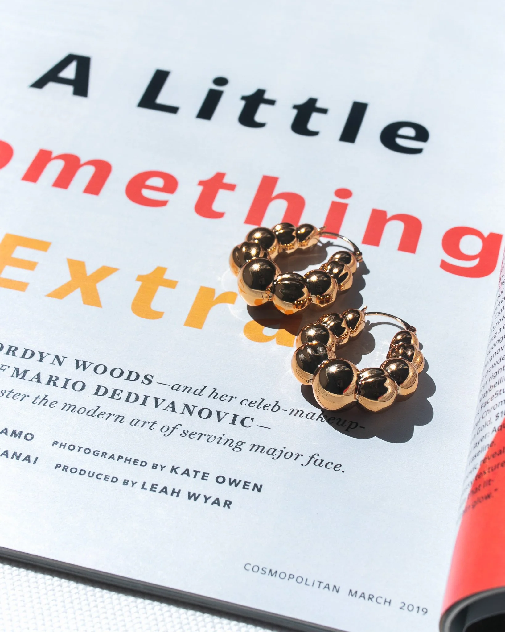 A pair of gold and black beaded hoop earrings resting on a magazine page with colorful text.