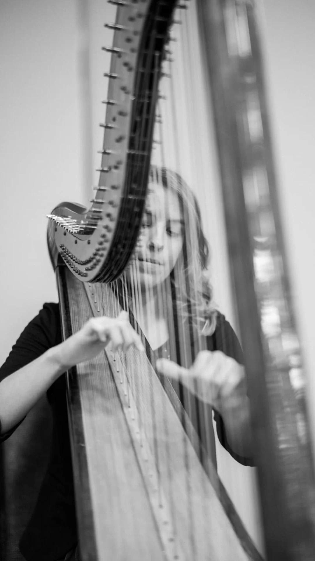 A woman playing a harp, seen through a glass reflection in a black and white photo.