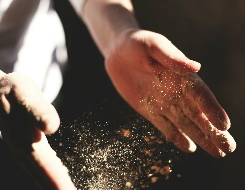 Close-up of hands sprinkling flour or powder onto a dark surface.