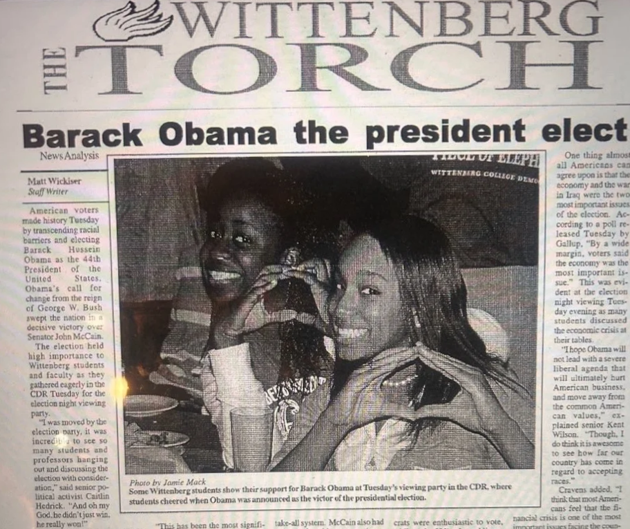 Black and white photo of two women, one with dark curly hair and the other with lighter straight hair, smiling and making a heart shape with their hands at a viewing party for Barack Obama's presidential election.