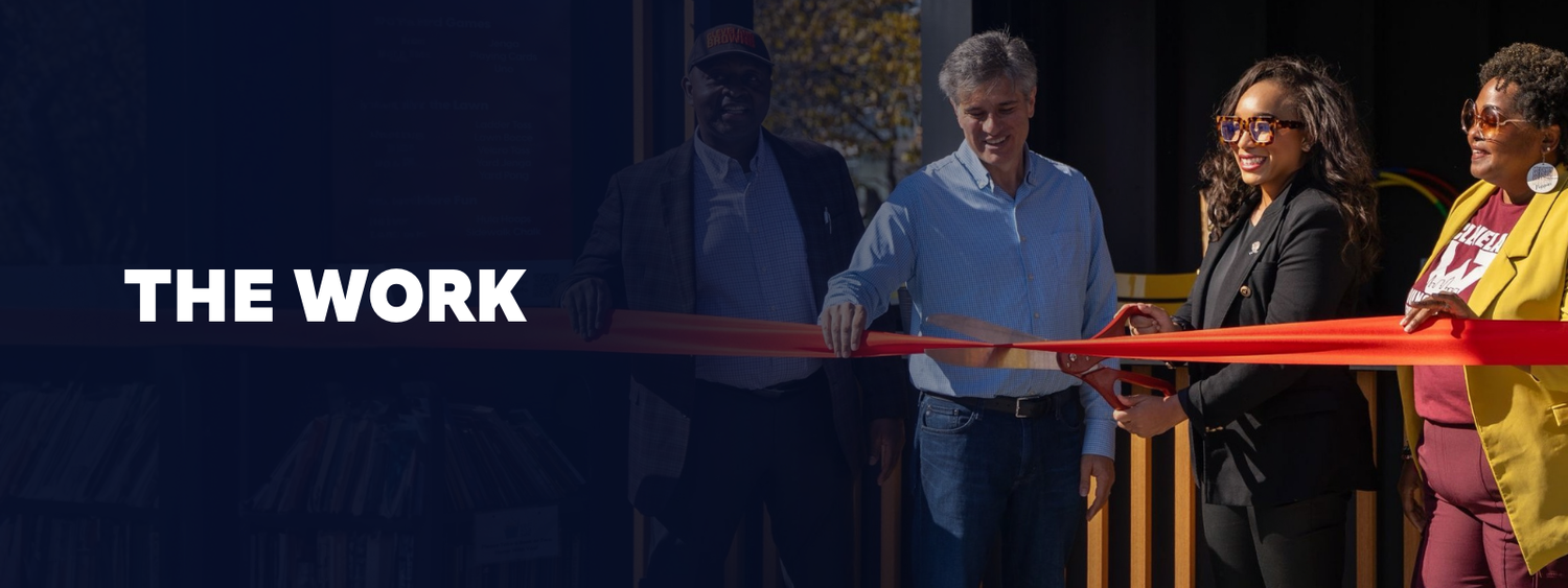 People participating in a ribbon-cutting ceremony outdoors, with the words "THE WORK" overlayed.