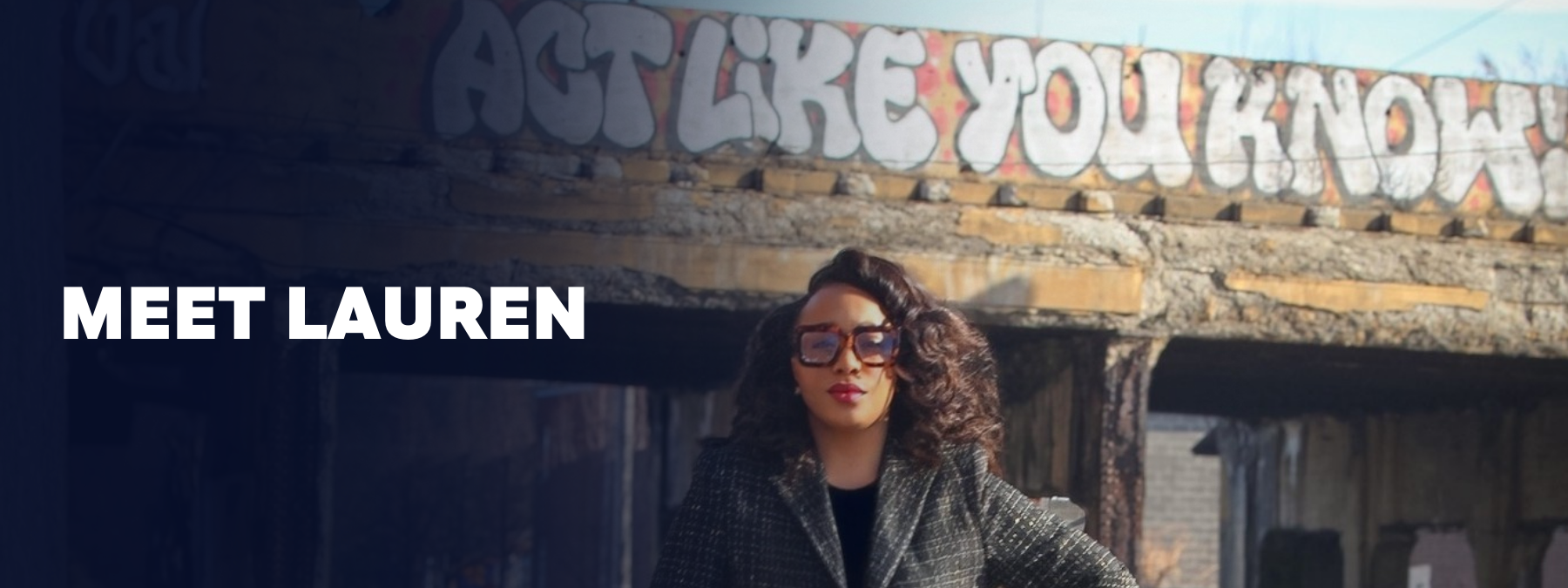 A woman with curly hair, sunglasses, and a blazer standing in front of a mural with graffiti that says 'JUST LIKE YOU KNOW' and the text 'MEET LAUREN' on the left side.