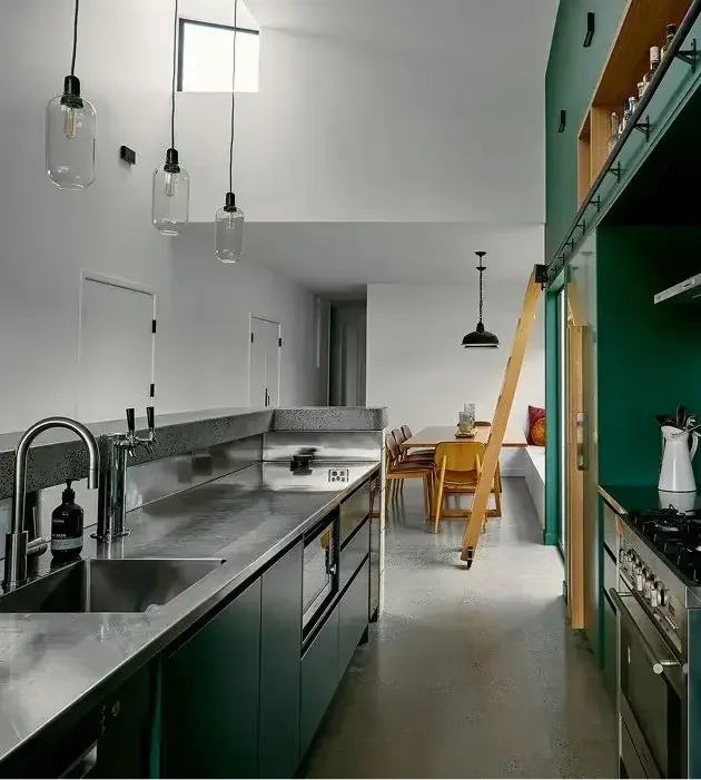 Modern kitchen with stainless steel countertops, pendant lights, a dining area with yellow chairs, and a green accent wall with cabinetry.