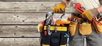 Person wearing gloves with a tool belt full of tools on a wooden surface
