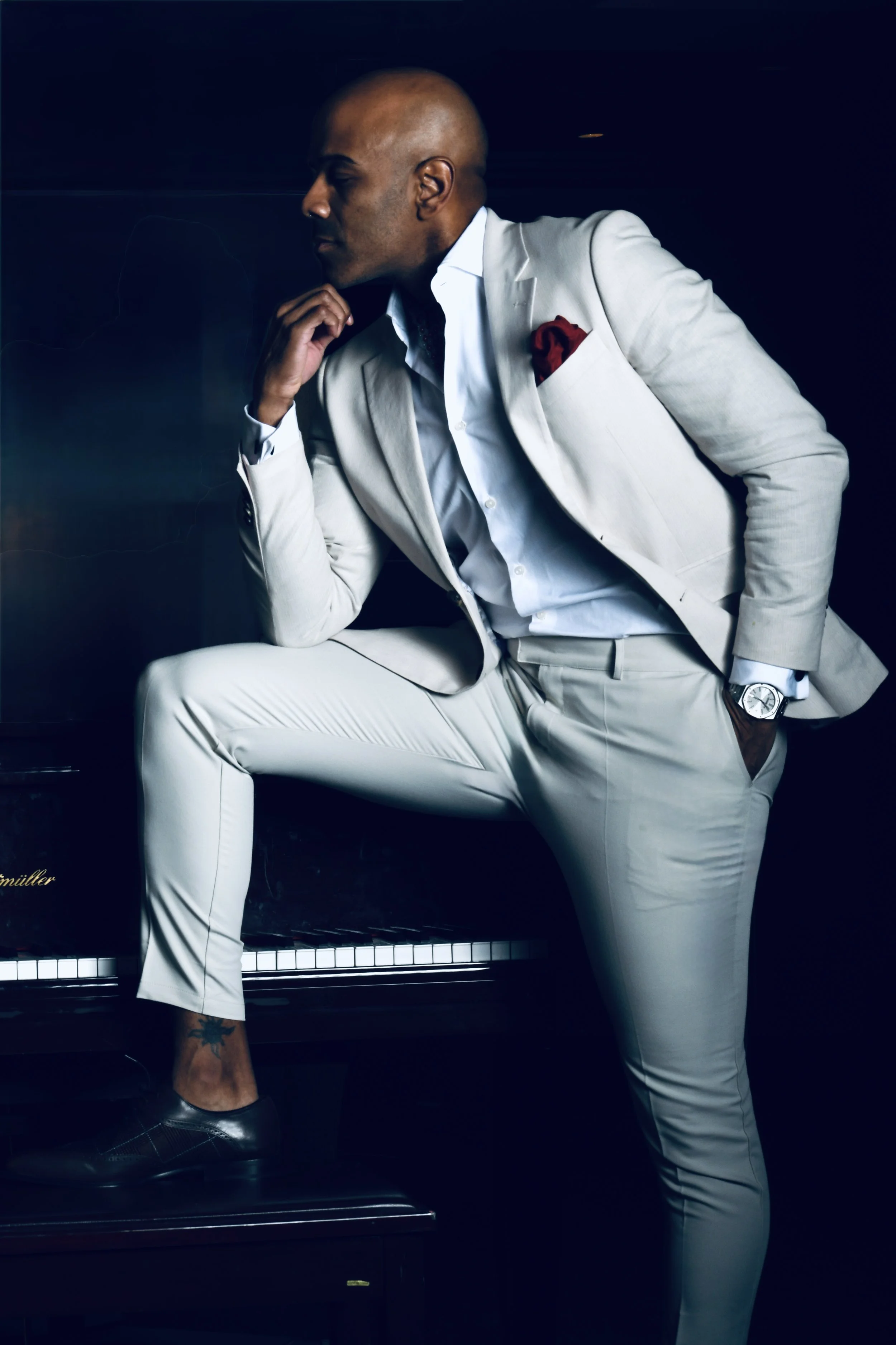 Sanjay Laforest a man in a white suit at a black grand piano, eyes closed, hand on the keys.
