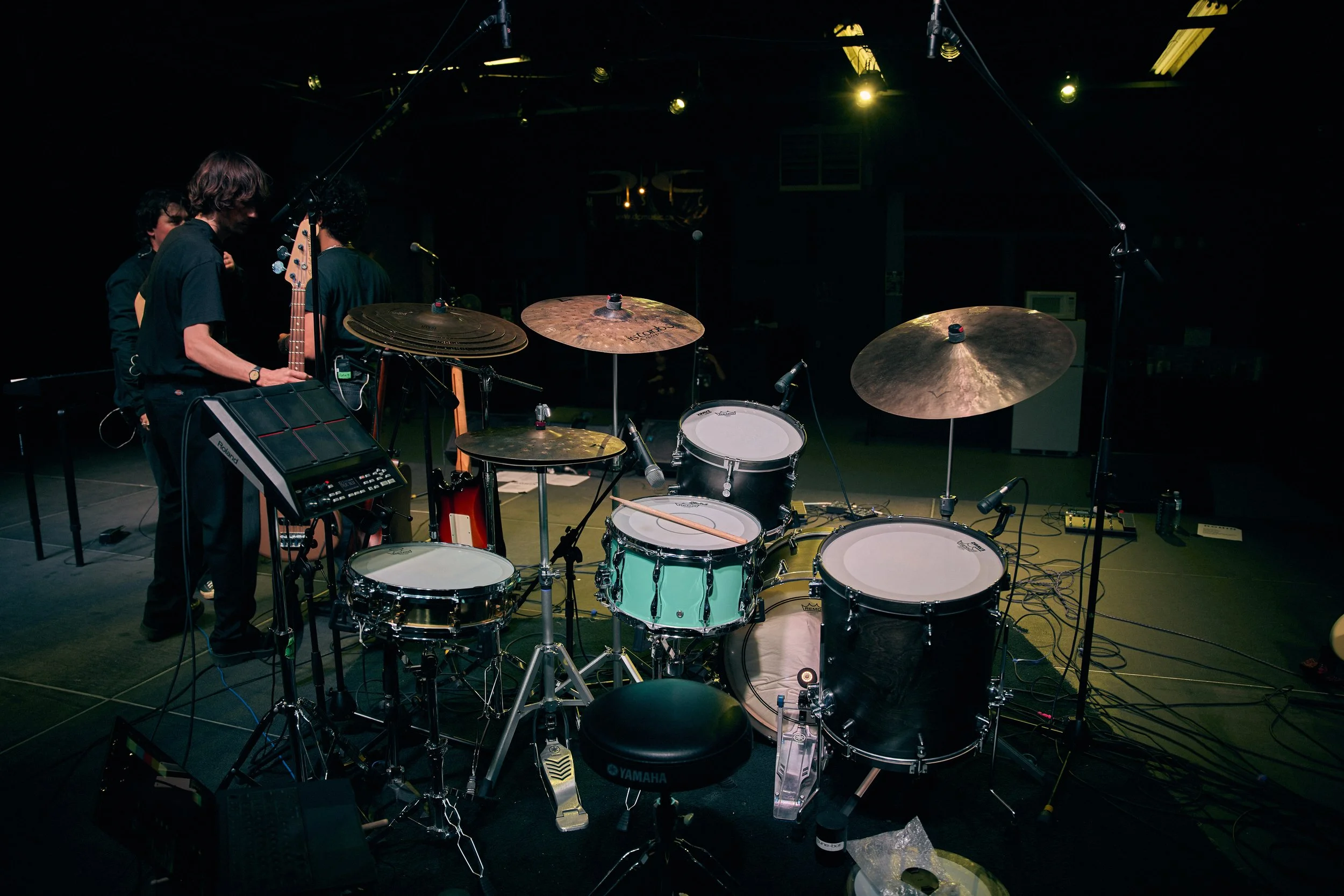 Drummer Miles Johnson's stage setup with a drum kit, cymbals, microphones, and several musicians preparing for a performance.
