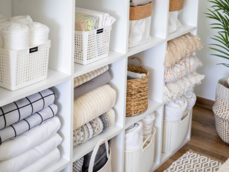 Organized shelves with towels, blankets, and storage bins in a neatly arranged linen closet.