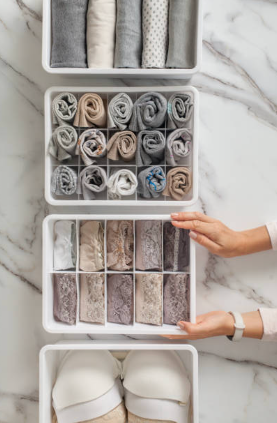 Open organized drawers containing rolled and folded socks and slippers on marble surface.