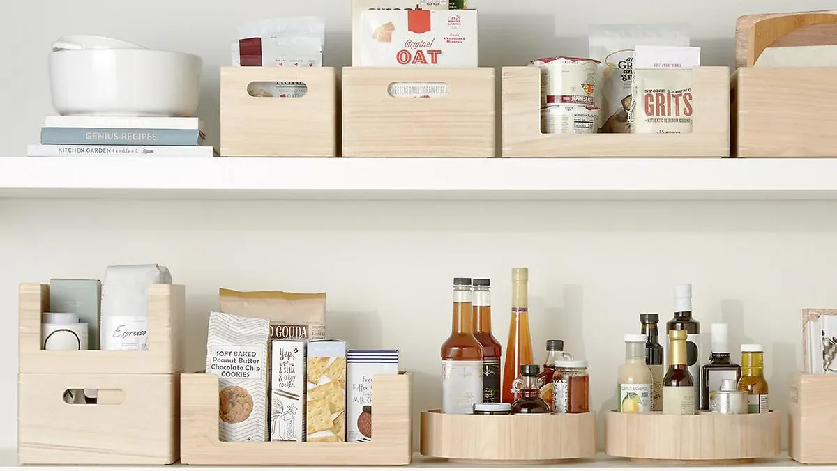 Kitchen shelves with food ingredients, spices, condiments, and cookbooks stored in wooden boxes.