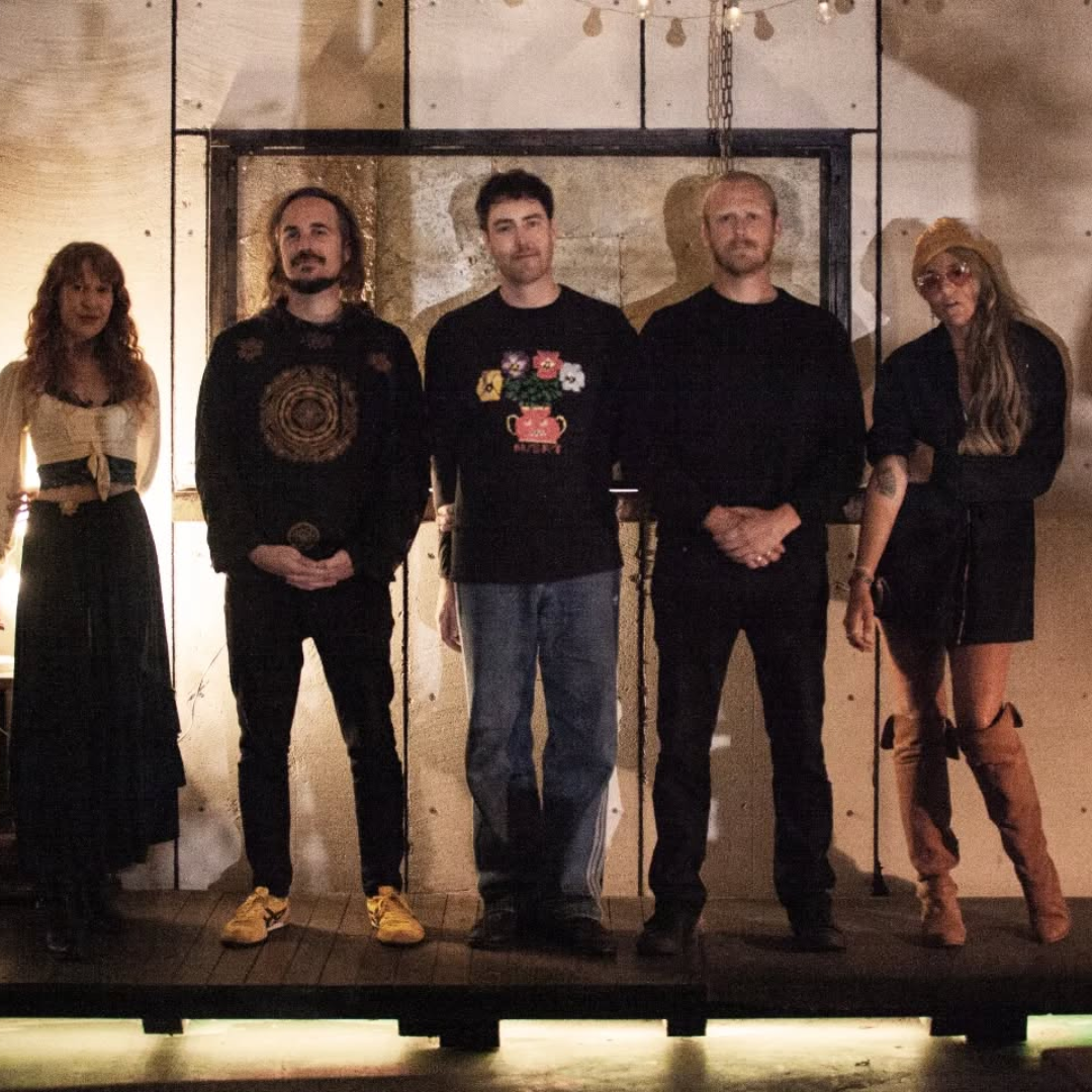 Five people standing side by side indoors with a wooden wall background.