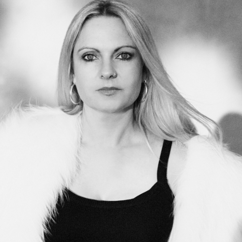 Black and white portrait of a woman with long straight hair, wearing hoop earrings, a black top, and a white fur coat.
