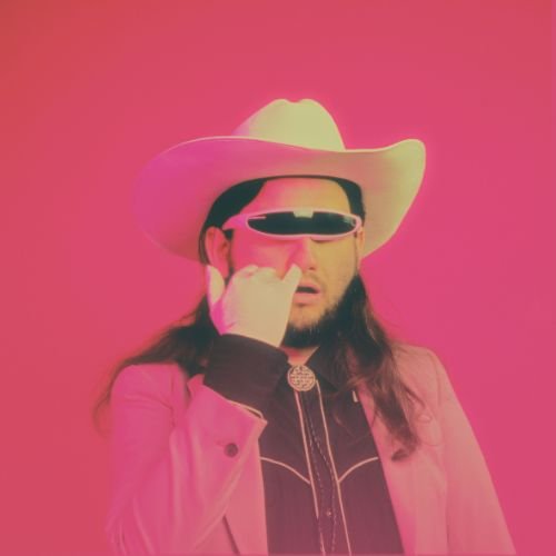 A man wearing a large cowboy hat, sunglasses, pink jacket, and shirt against a pink background.