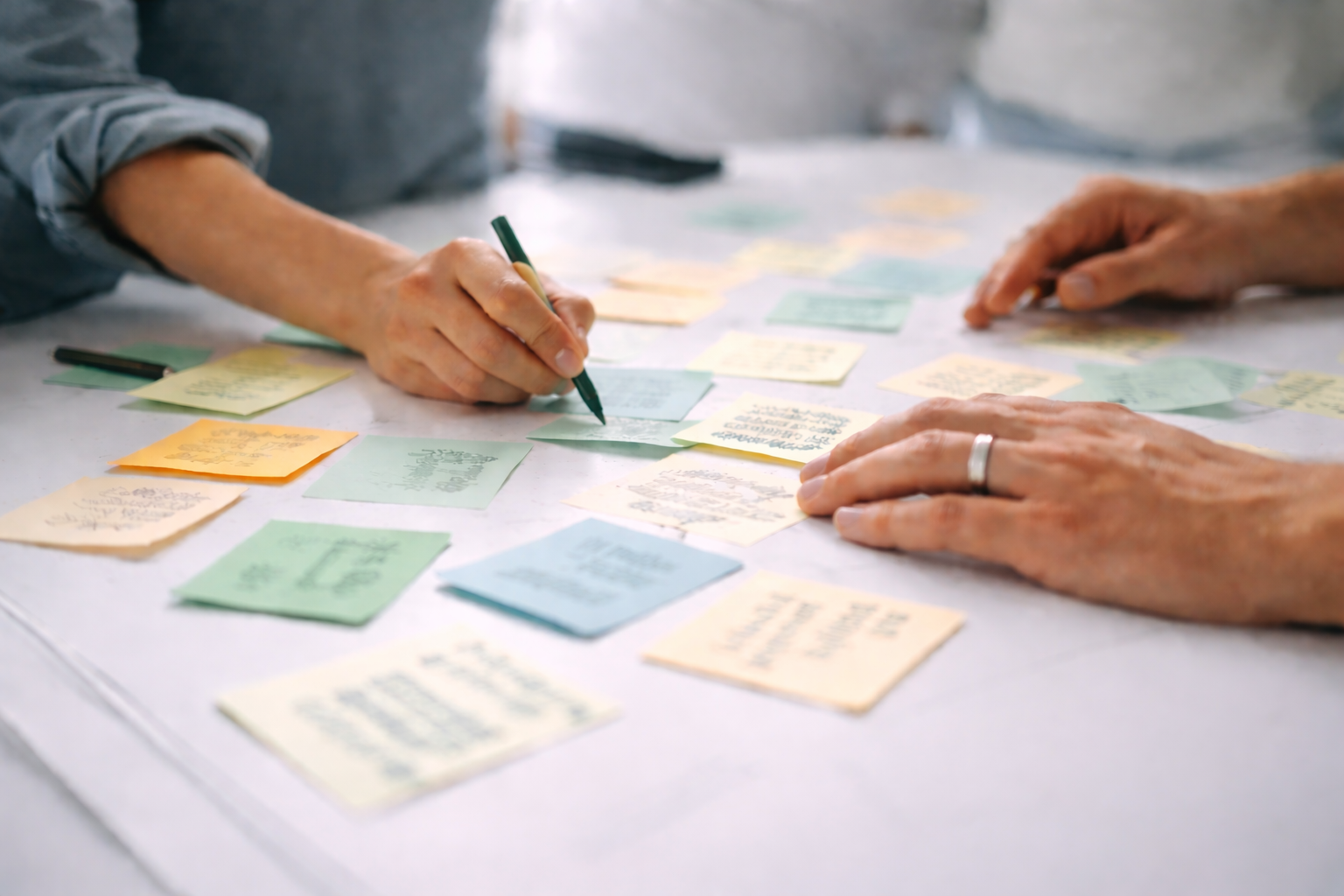 Two people organizing and writing on colorful sticky notes spread across a white table.