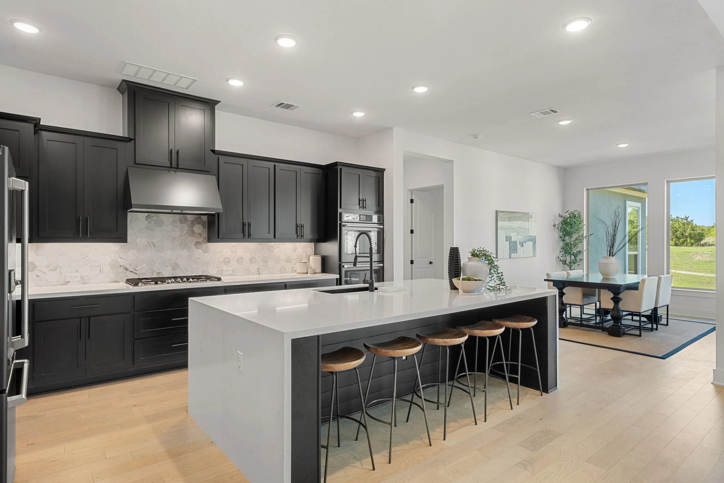Modern kitchen with dark cabinetry, waterfall island, wood floors, stainless appliances, open concept layout.