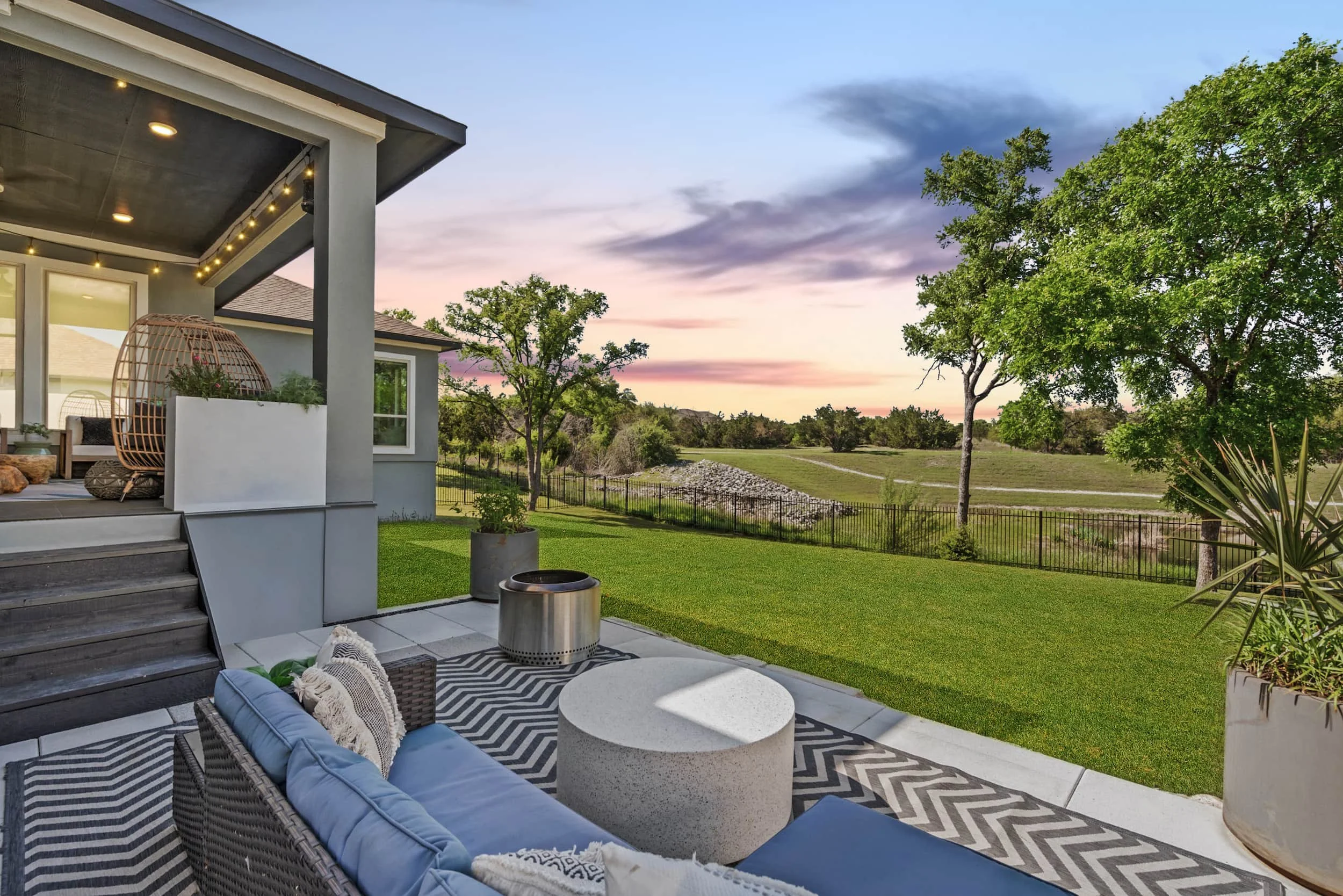 Modern backyard patio staged with blue outdoor sofa, concrete table, and string lights.