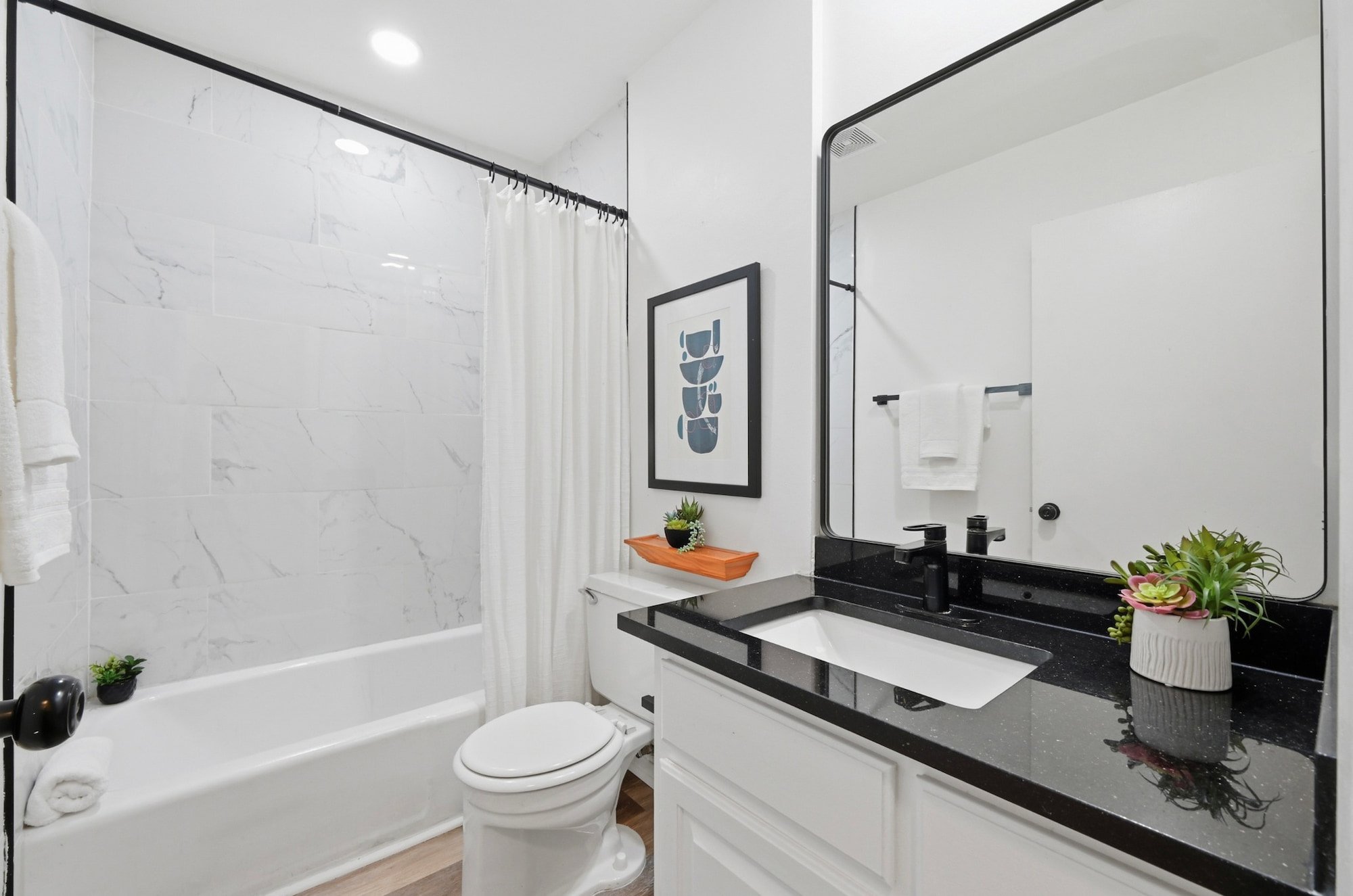 A marble-tiled tub surround pairs with black fixtures and framed abstract art.