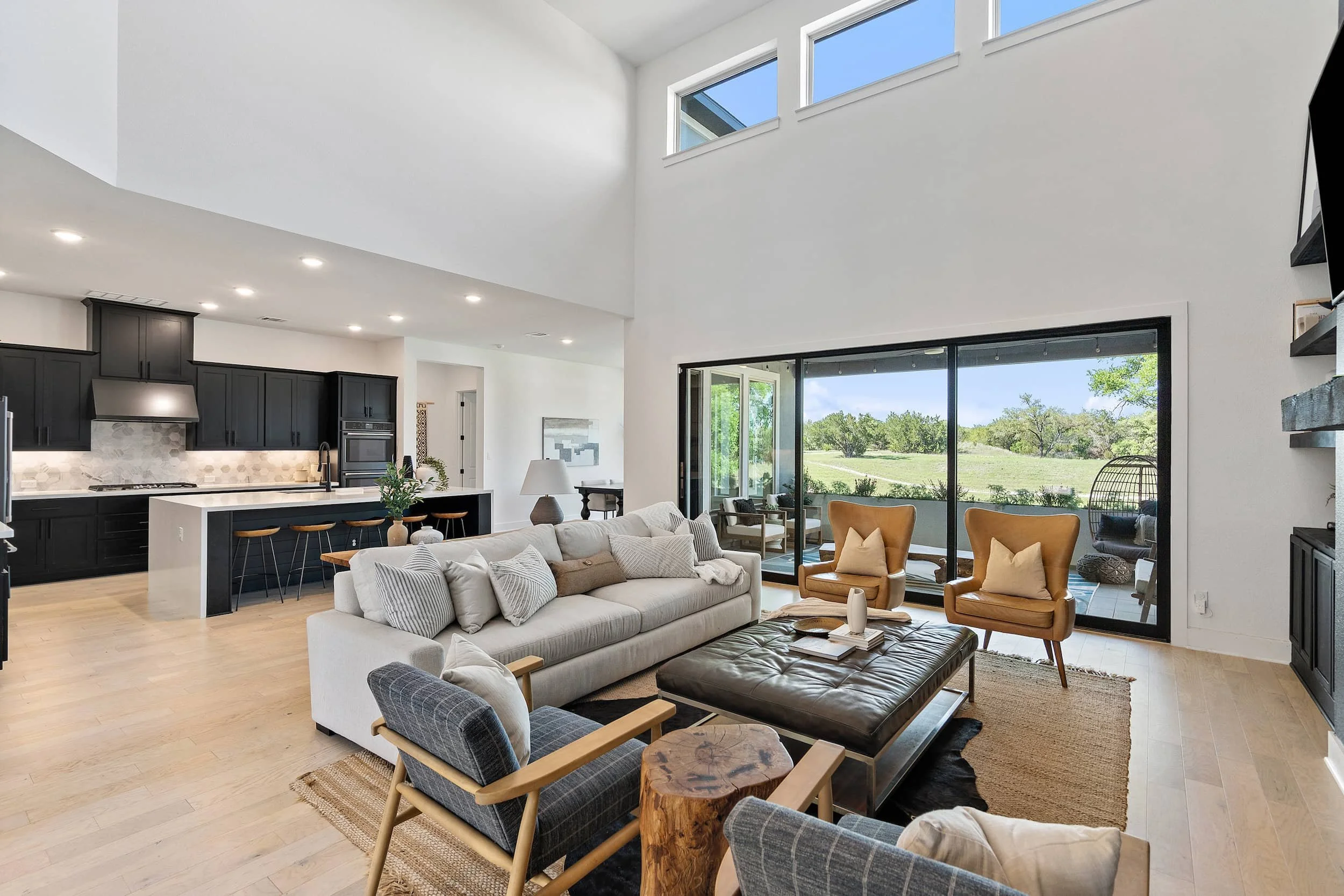Austin open living room staging with large windows, sliding glass doors, neutral sofa, leather chairs, indoor outdoor flow.