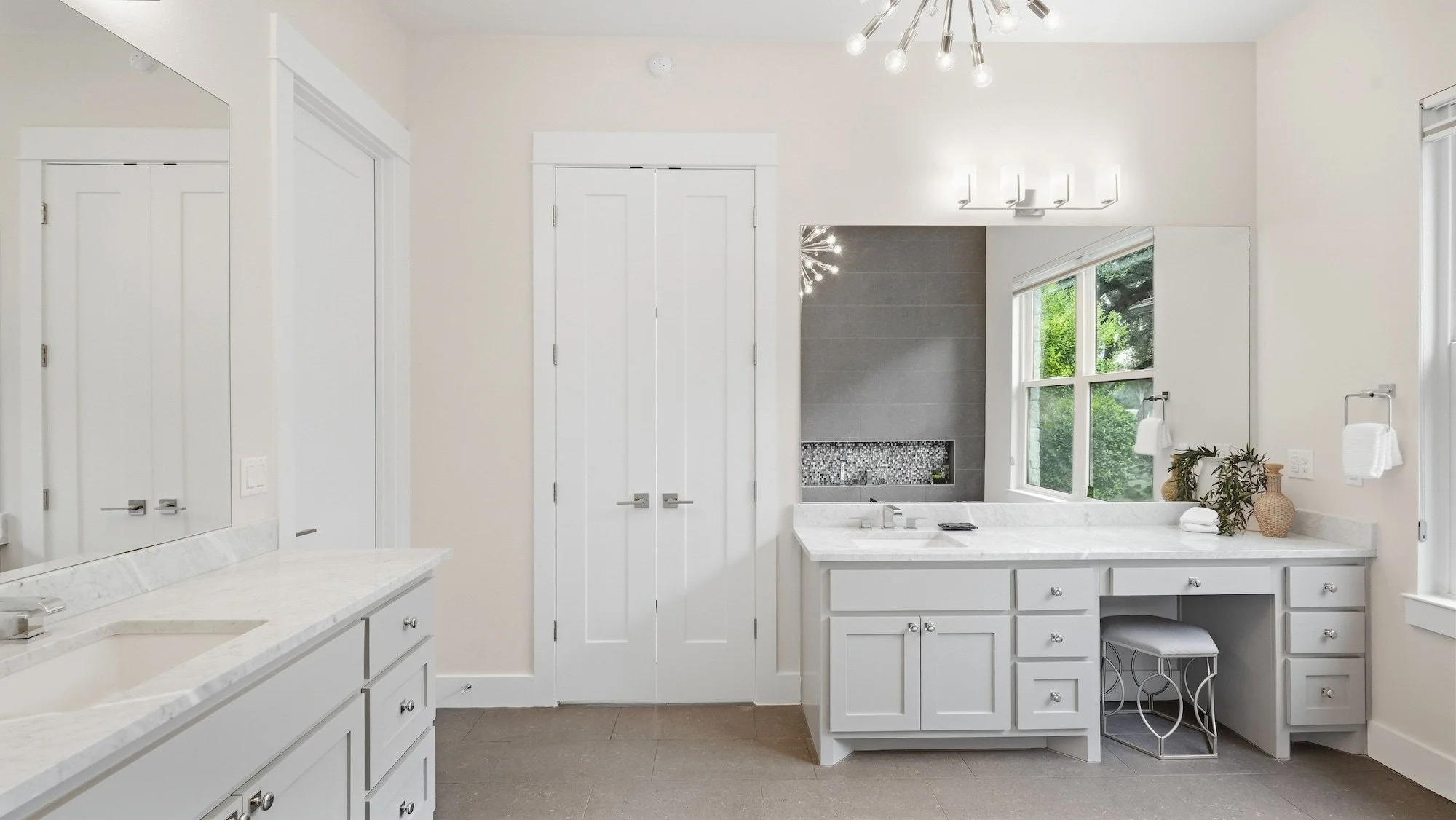 Primary bathroom staged with dual marble vanities, a makeup station with a silver stool, and a sputnik chandelier.