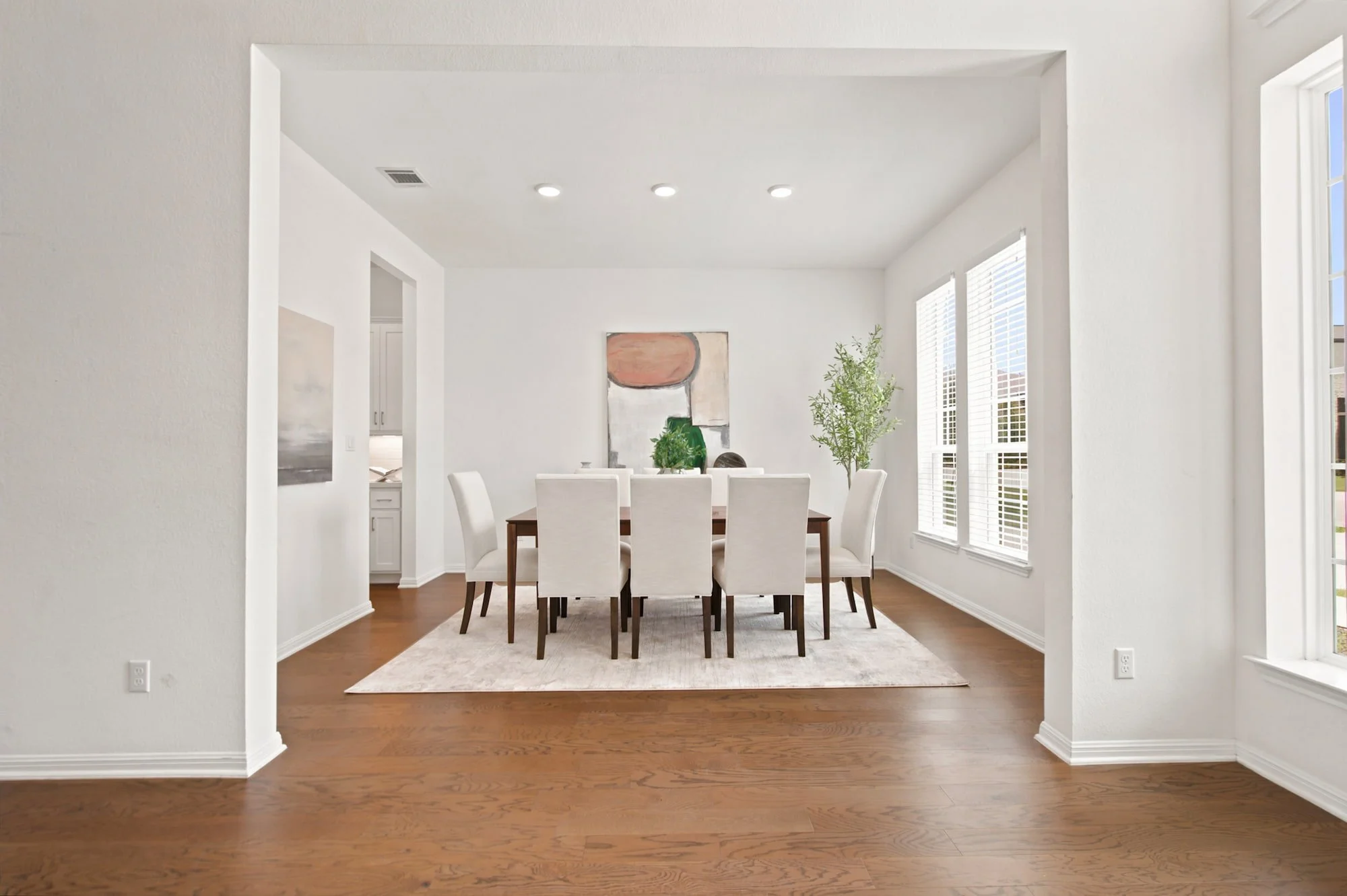 Dining room staged with a wood table, cream upholstered chairs, and layered abstract art.