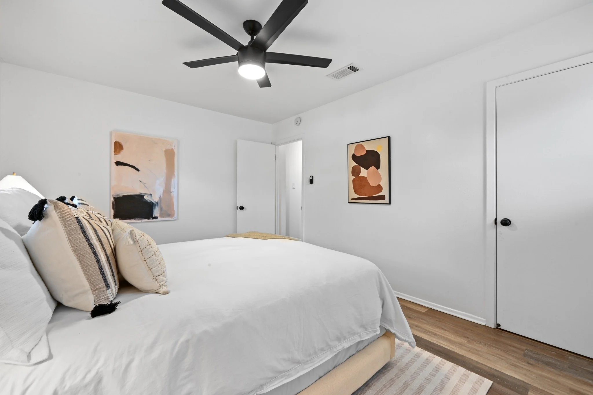 Secondary bedroom staged with a black ceiling fan, neutral bedding, and abstract wall art.