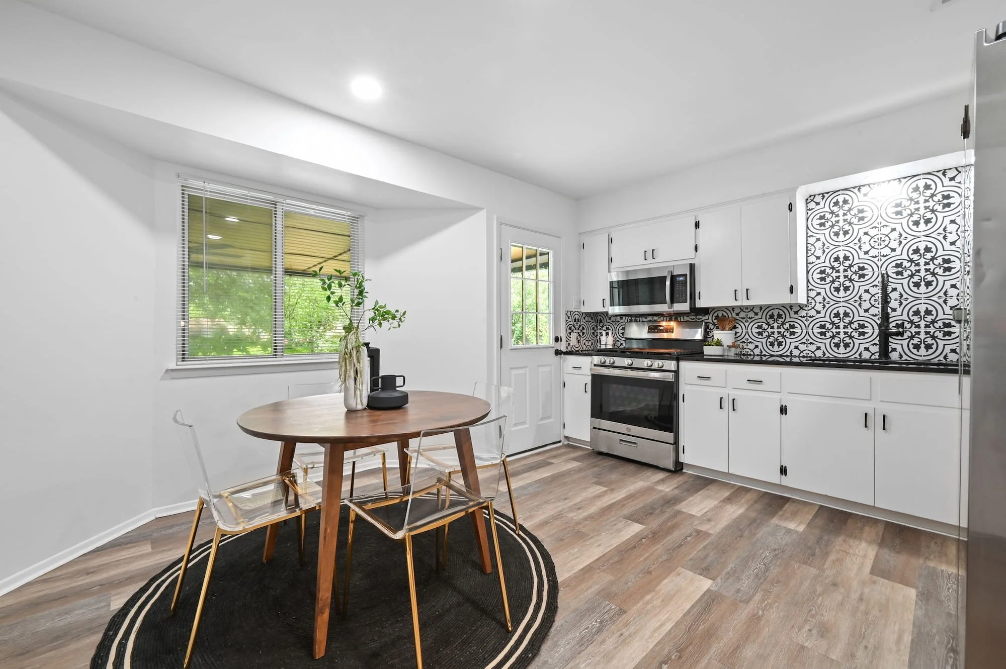 Open dining nook with round wood table leads into a staged kitchen with patterned tile backsplash.cool