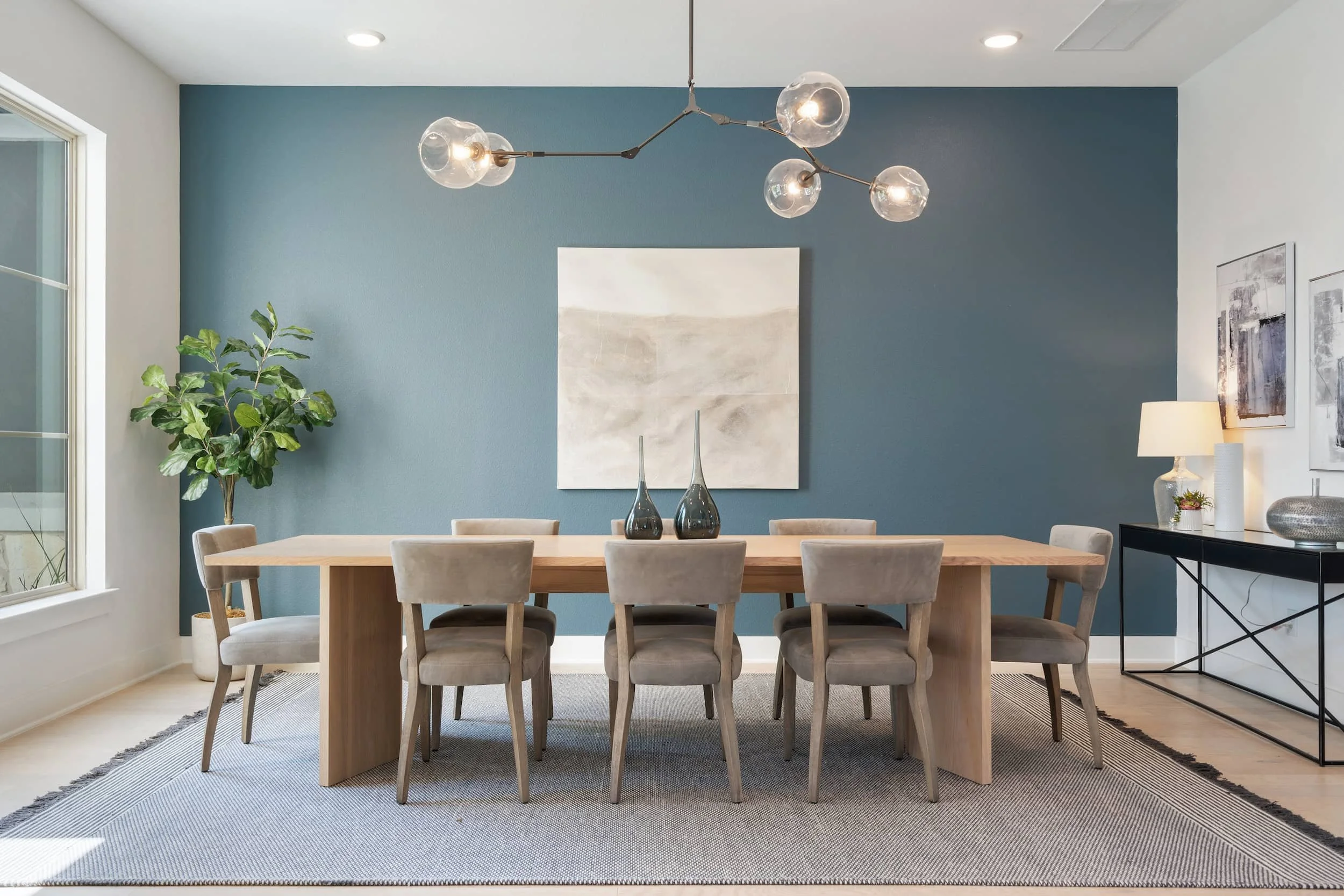 Contemporary dining room staging with natural wood furniture, glass chandelier, neutral decor, bold wall color in Austin.