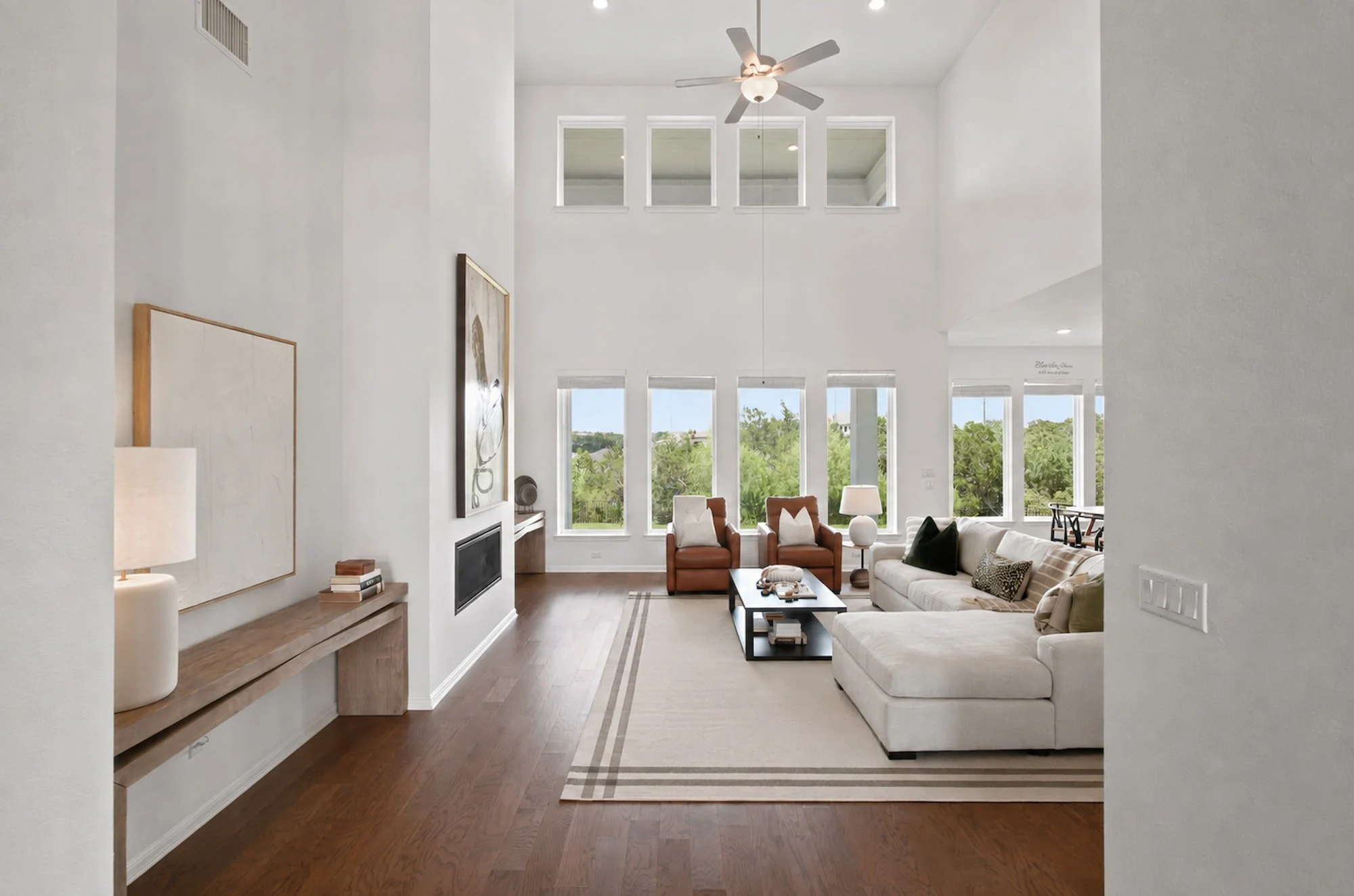 Leather chairs and a sectional anchor the two-story living room beneath tall windows.
