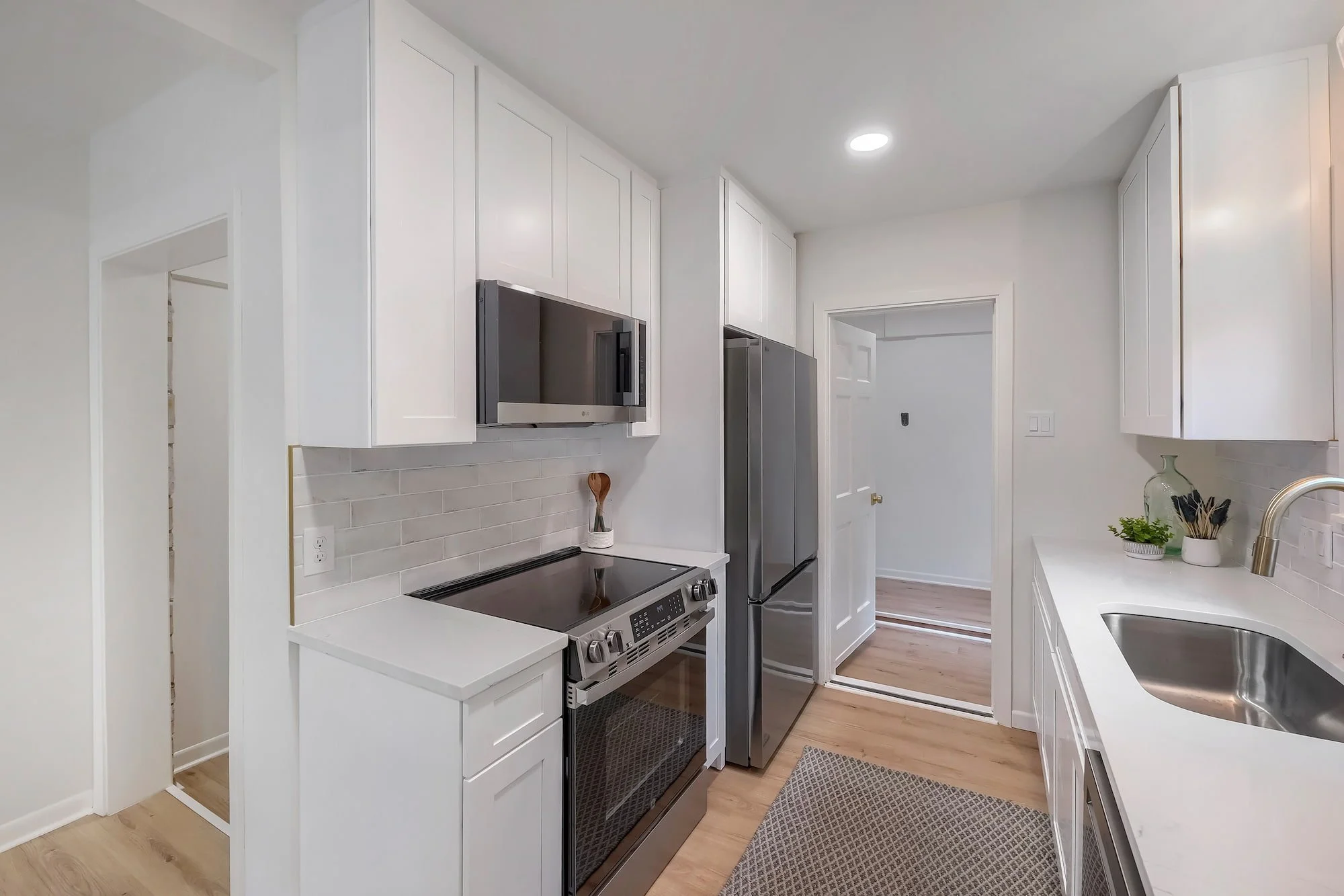 Bright galley kitchen featuring quartz countertops, shaker cabinetry, and stainless steel appliances