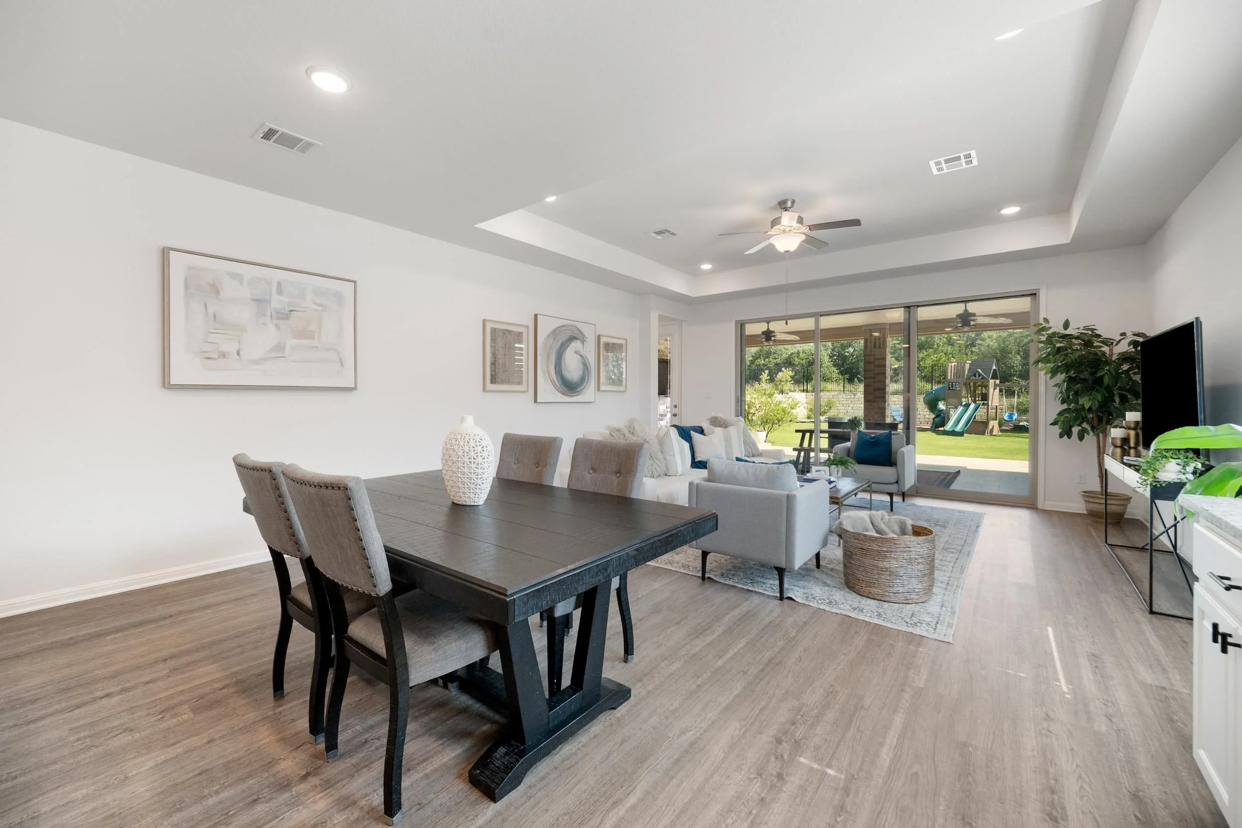 Interior view of a staged dining room and living area with wood floors, neutral decor, and large sliding glass doors.