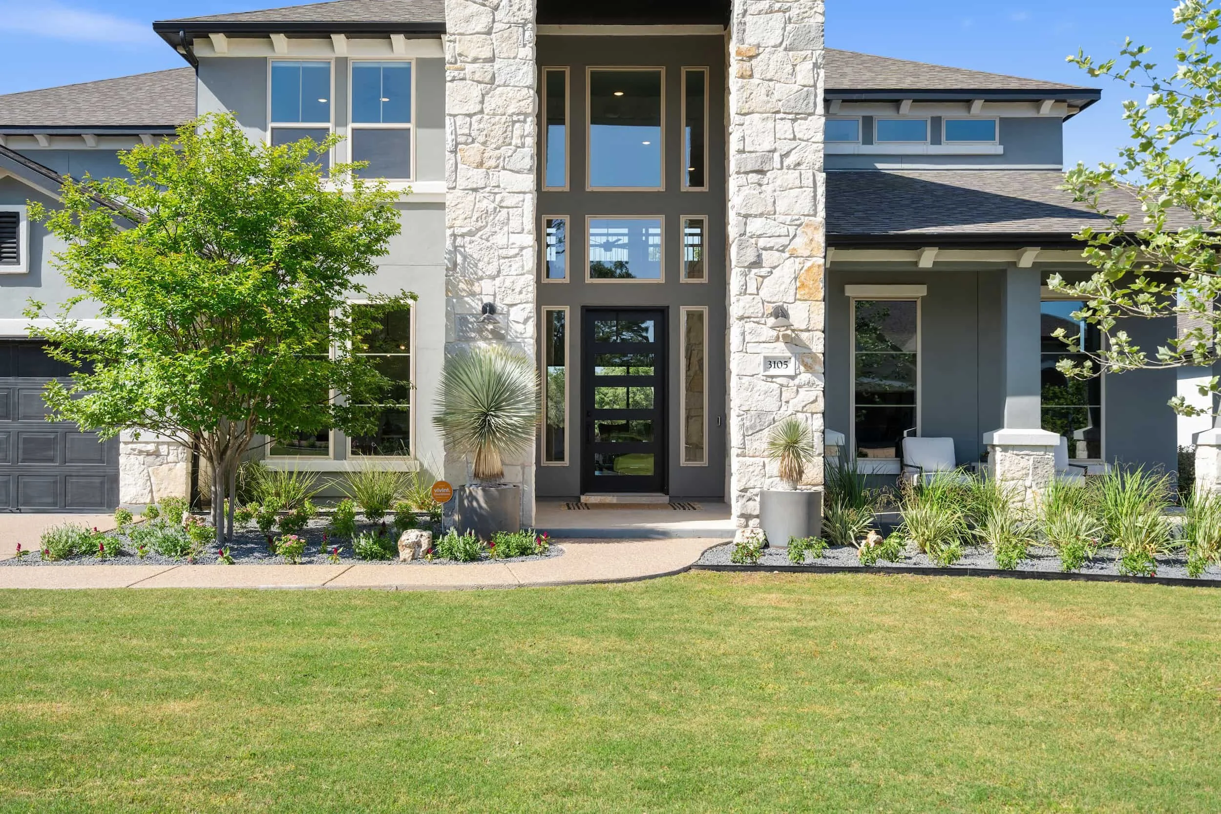 Staged modern Austin home exterior with stone pillars, dark front door, fresh landscaping, and lush green curb appeal.