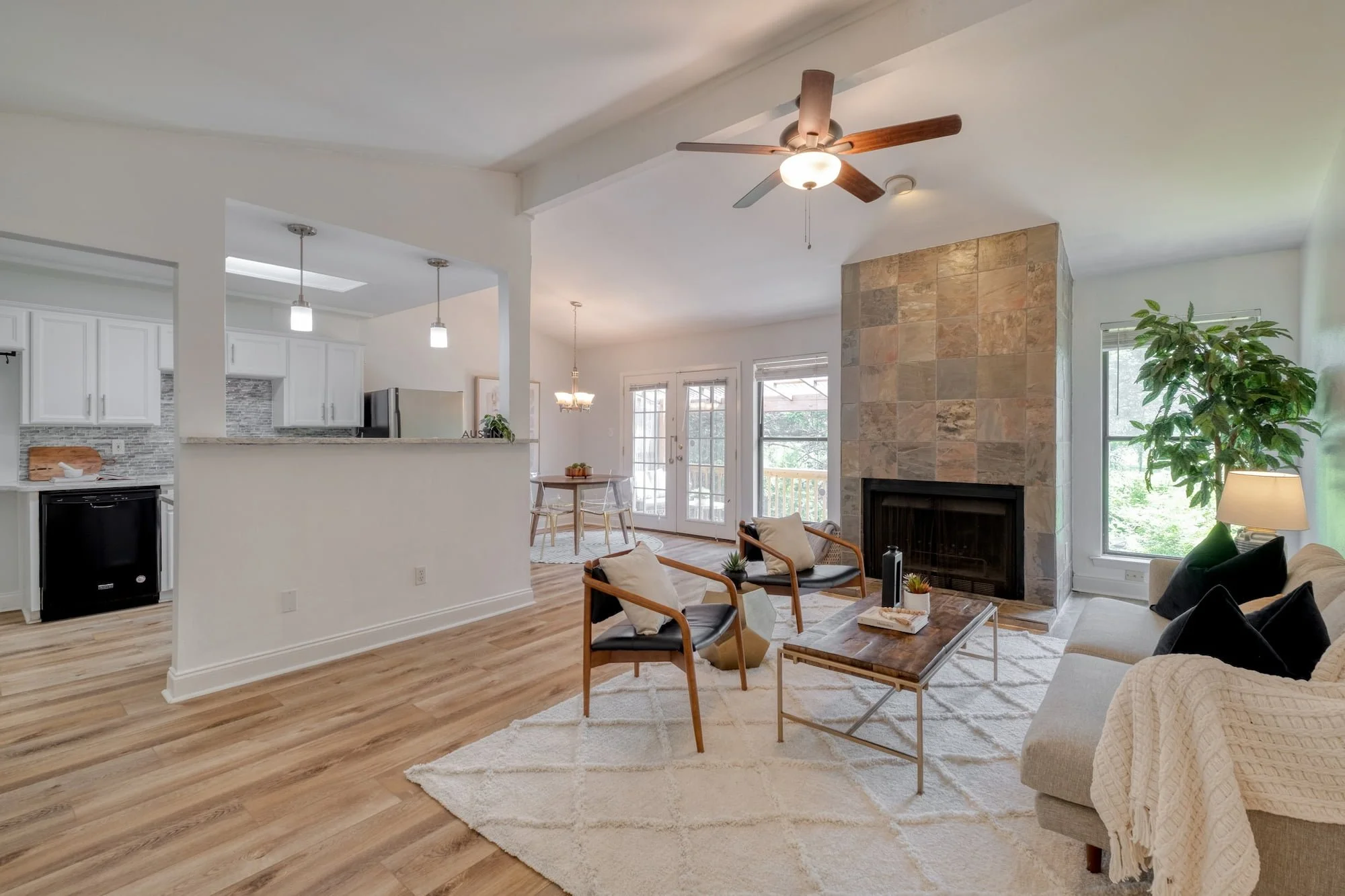 Open-concept living and dining area with vaulted ceilings, stone fireplace, and contemporary staging.