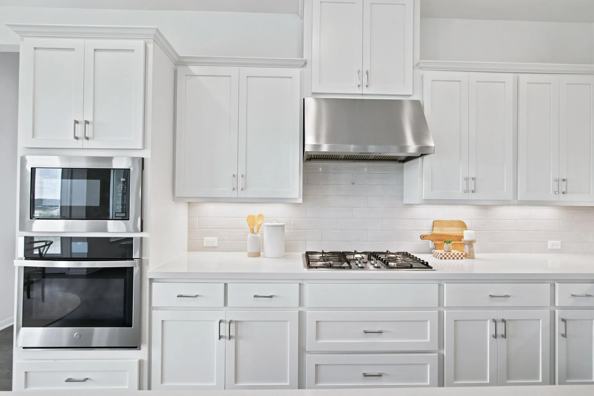 A stainless range and hood are flanked by white cabinetry and a tiled backsplash.