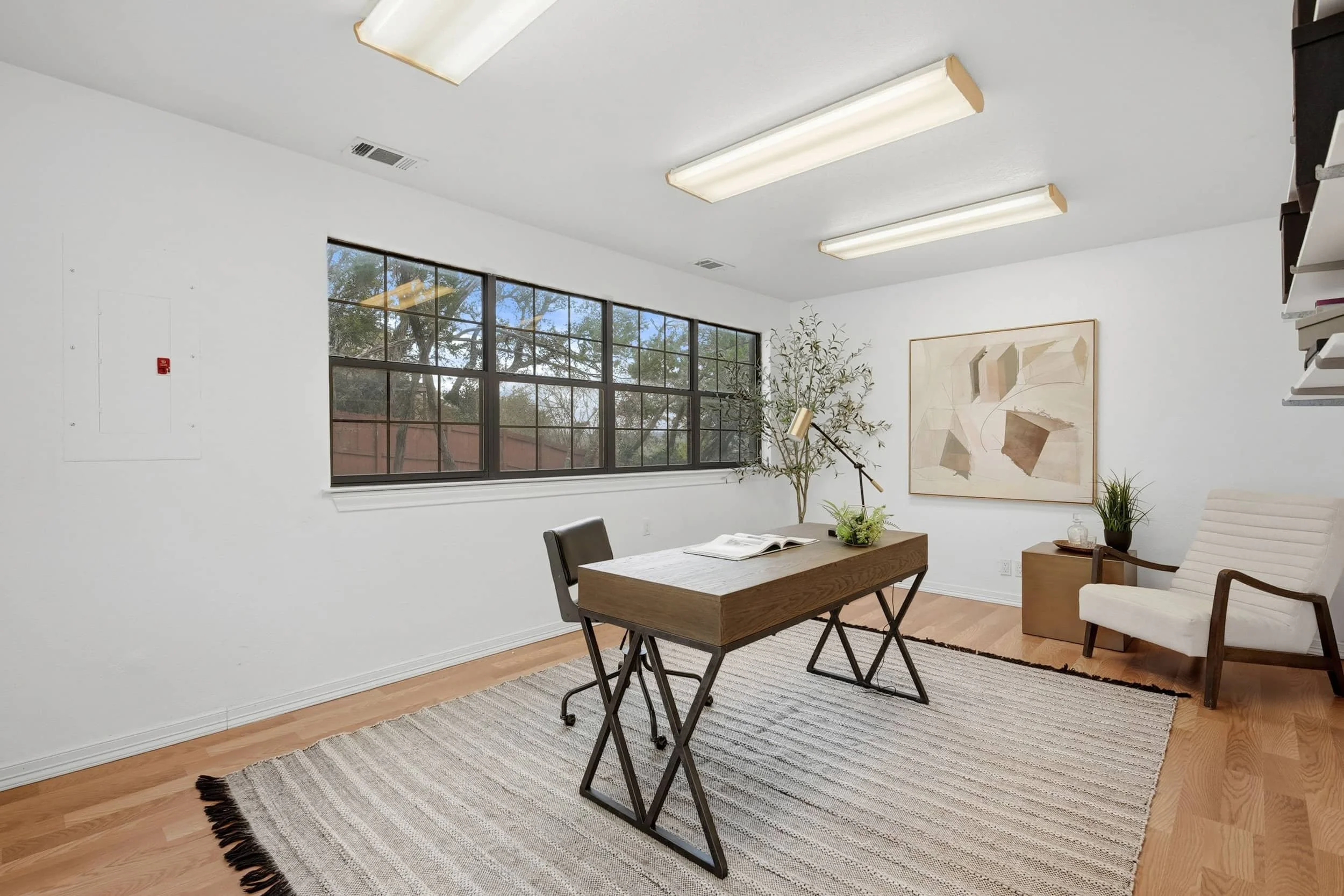 Elegant home office with wood desk, accent chair, large window, and neutral decor.