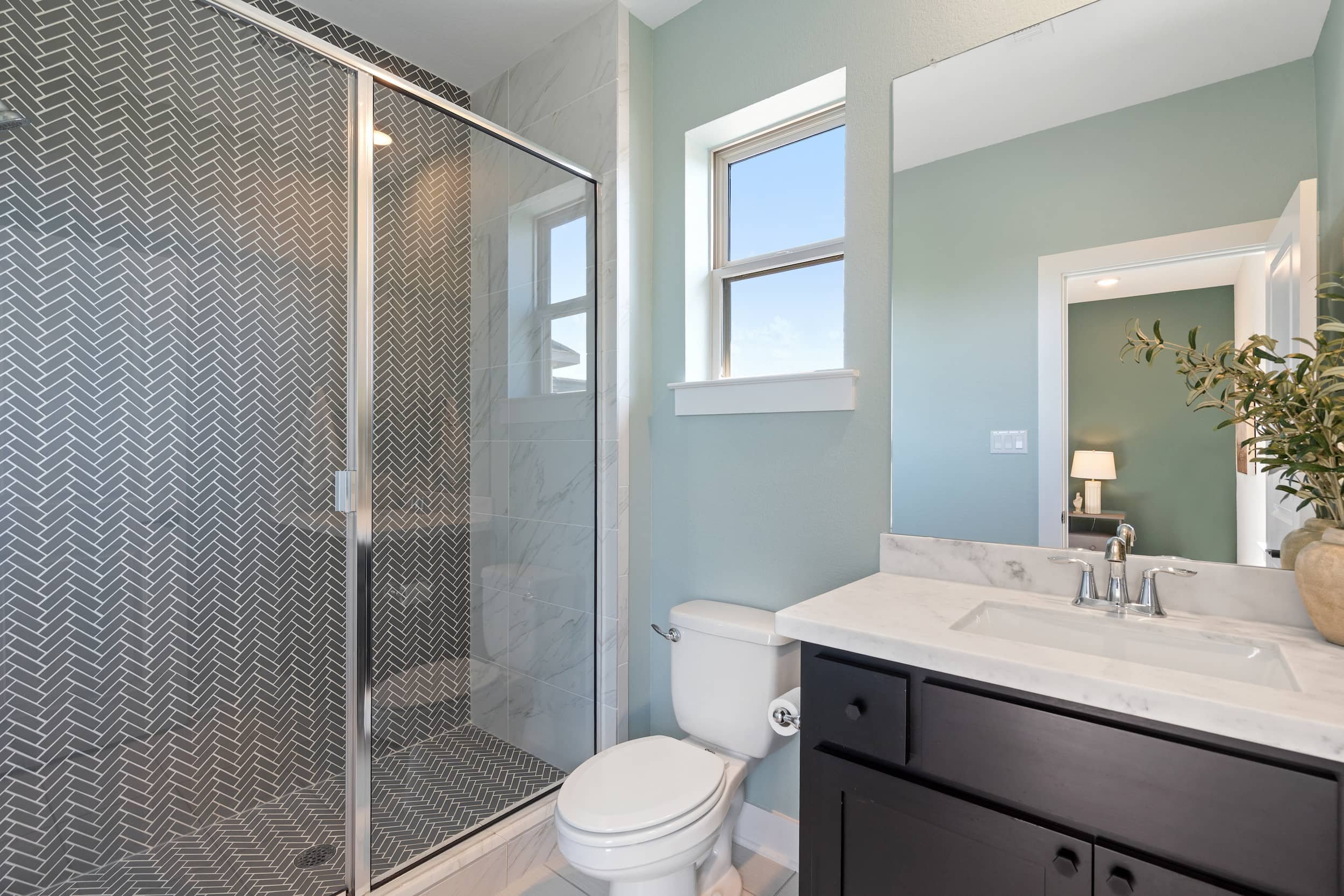 Contemporary staged bathroom featuring glass shower, patterned tile, single vanity, chrome fixtures.