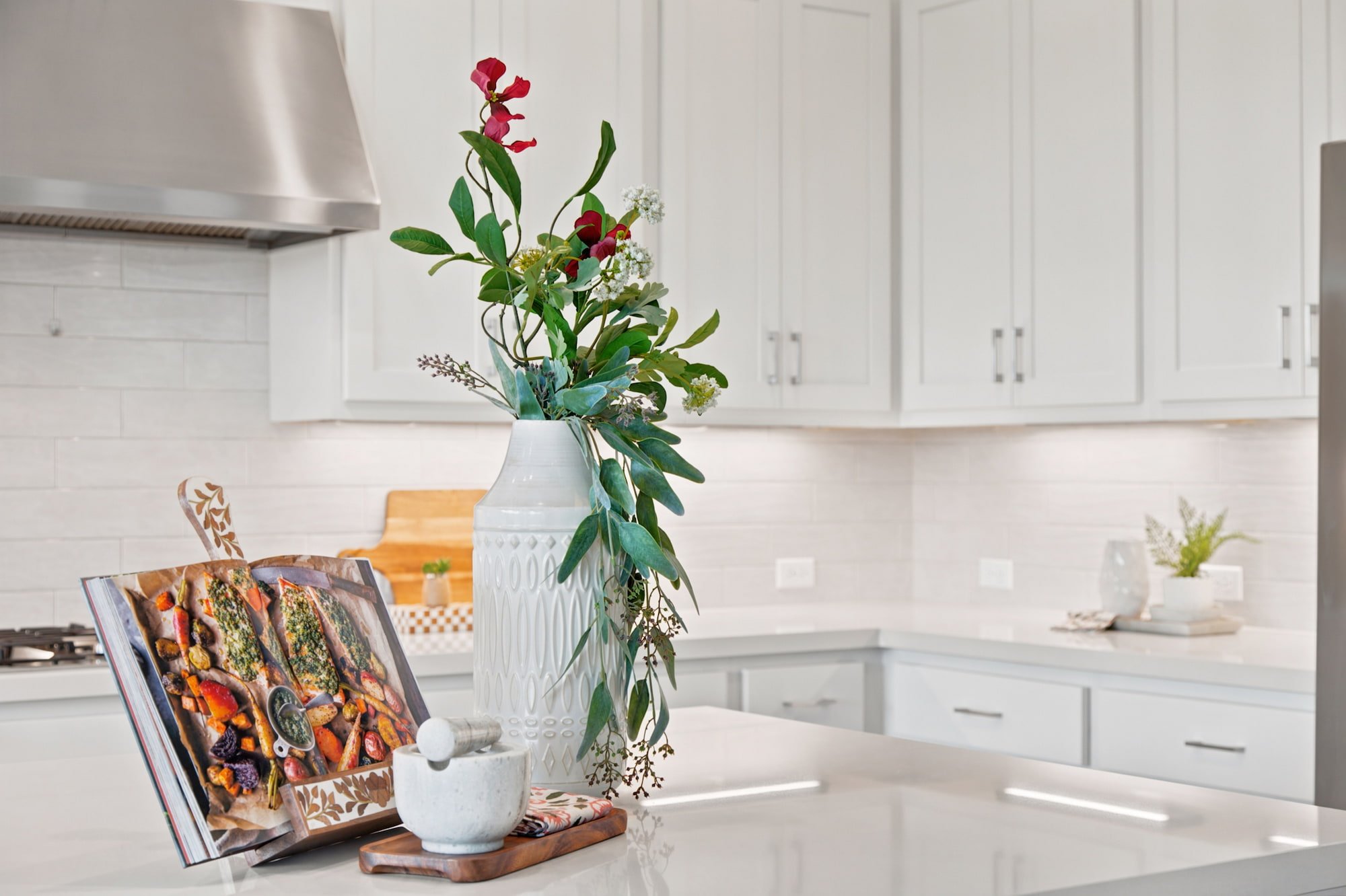 A textured vase with greenery and a cookbook style the white quartz counter.